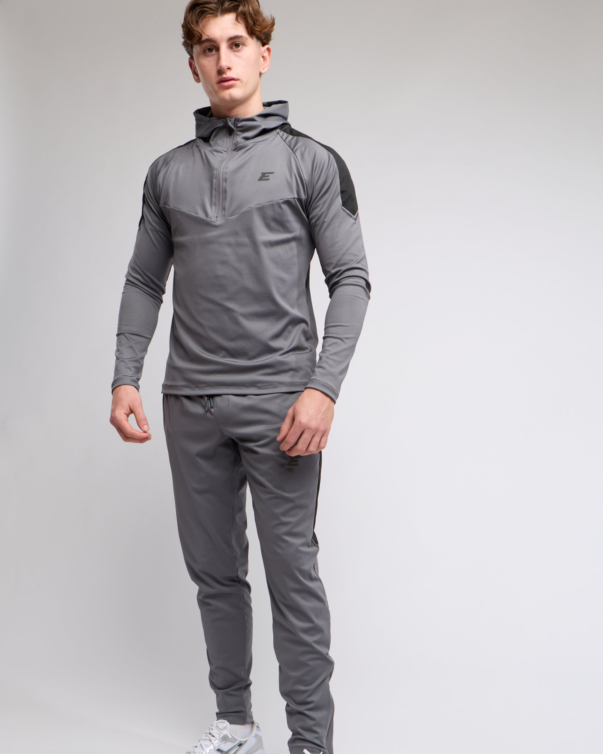Person wearing a gray tracksuit set with a brand logo on a light gray background