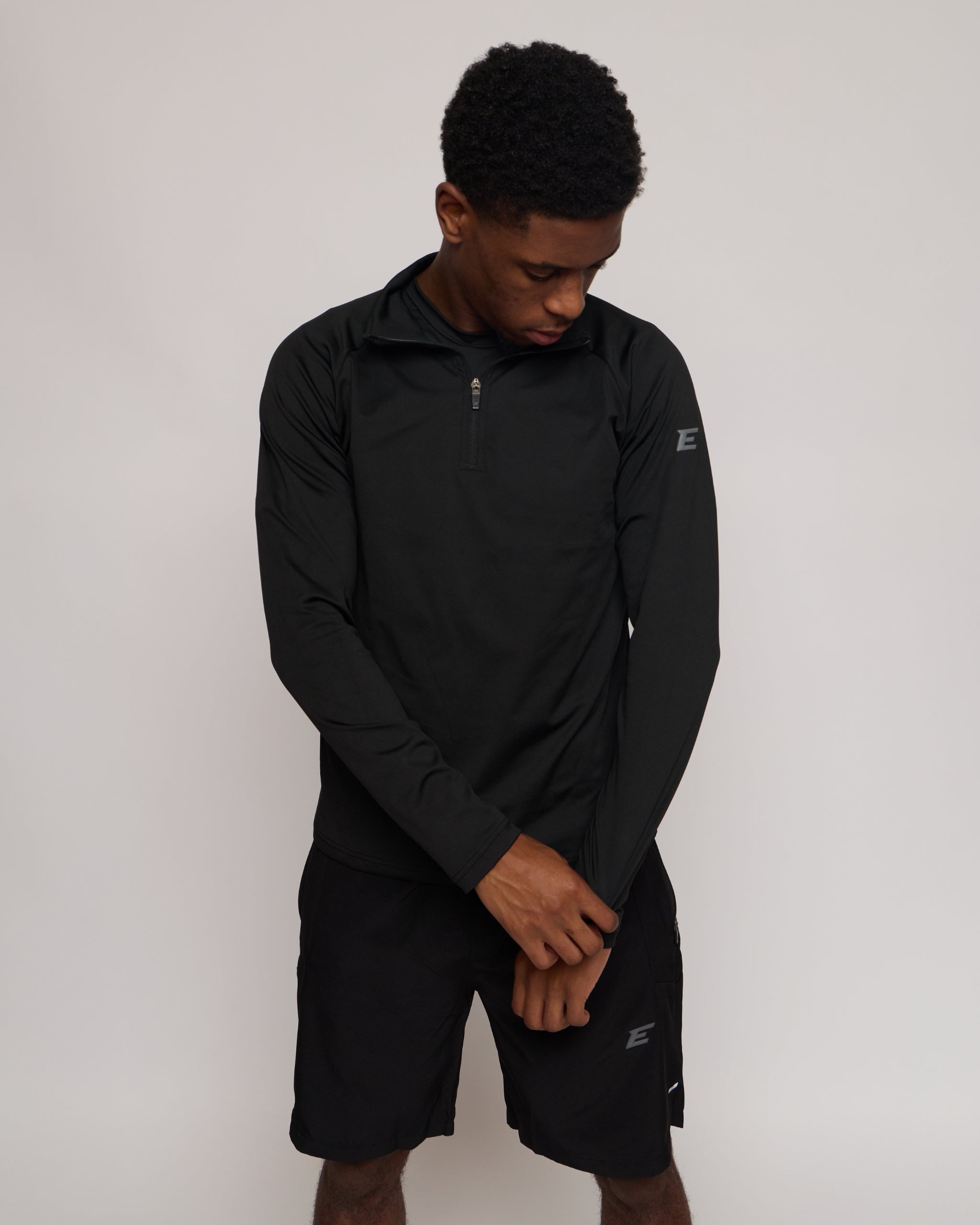 Man wearing a long sleeve black athletic quarter zip top with a white 'E' logo with matching shorts on a light background