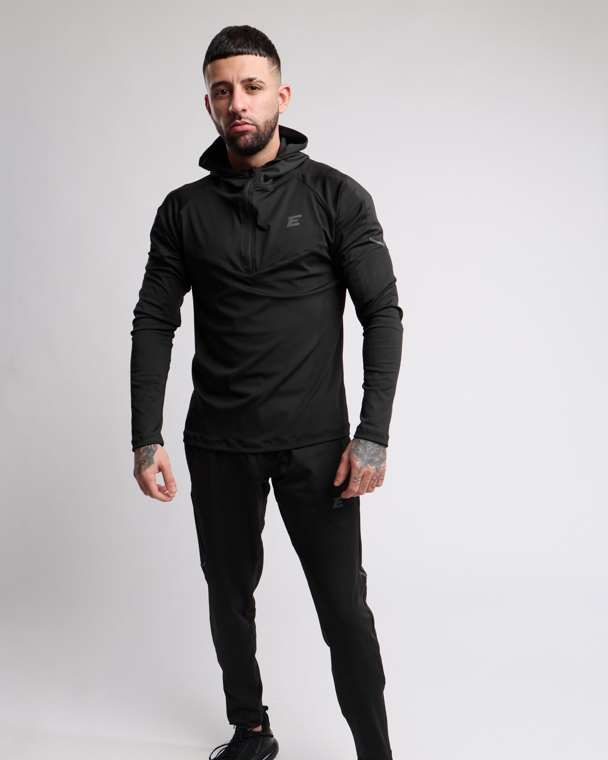 Man wearing a black athletic zip top and bottoms set with elegante brand logo on a white background
