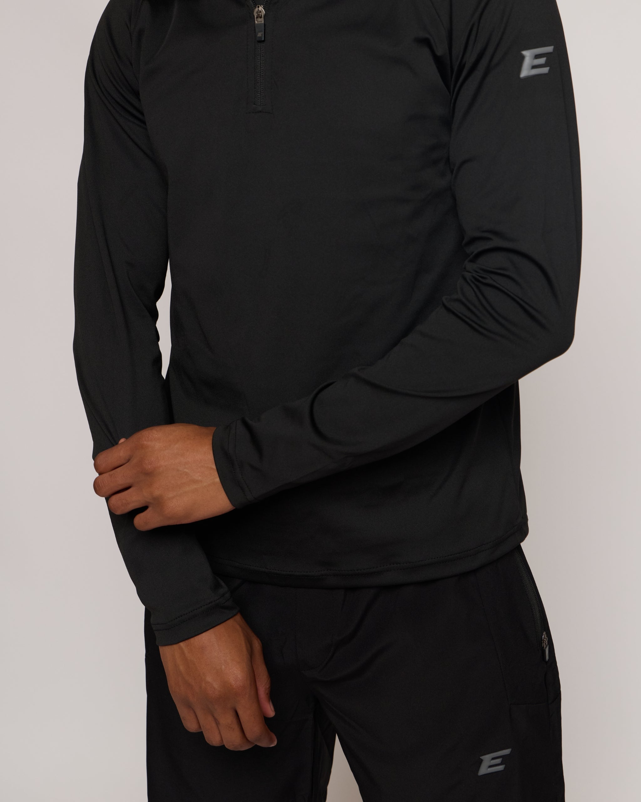 Man wearing a long sleeve black athletic quarter zip top with a white 'E' logo with matching shorts on a light background
