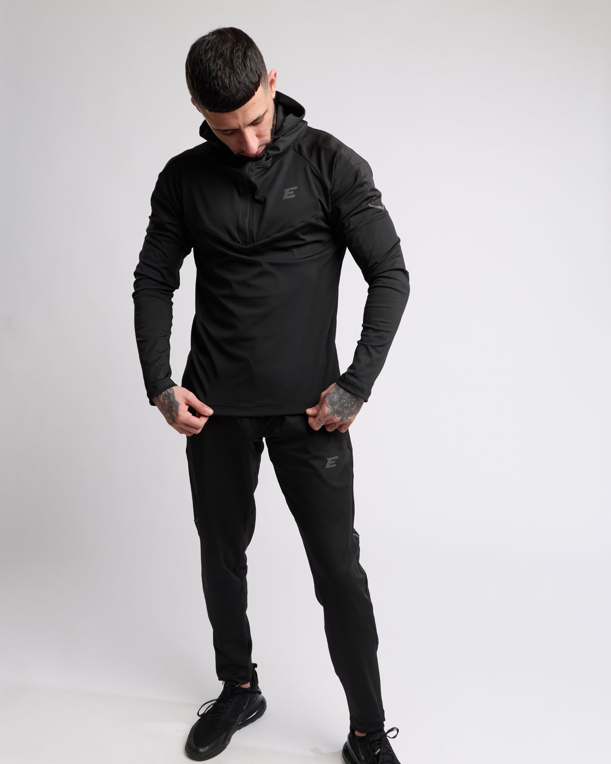 Man wearing a black athletic zip top and bottoms set with elegante brand logo on a white background