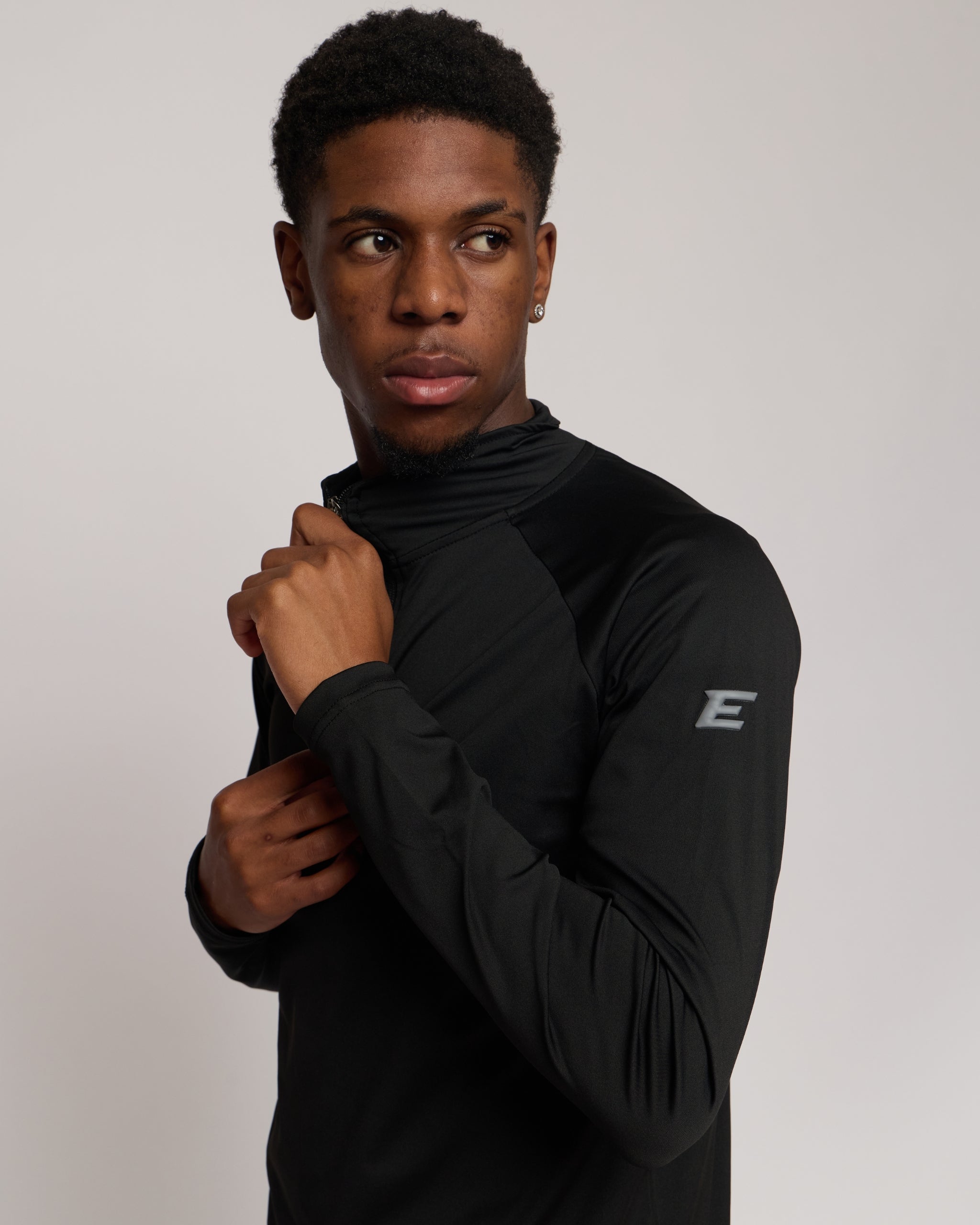 Man wearing a long sleeve black athletic quarter zip top with a white 'E' logo on a light background
