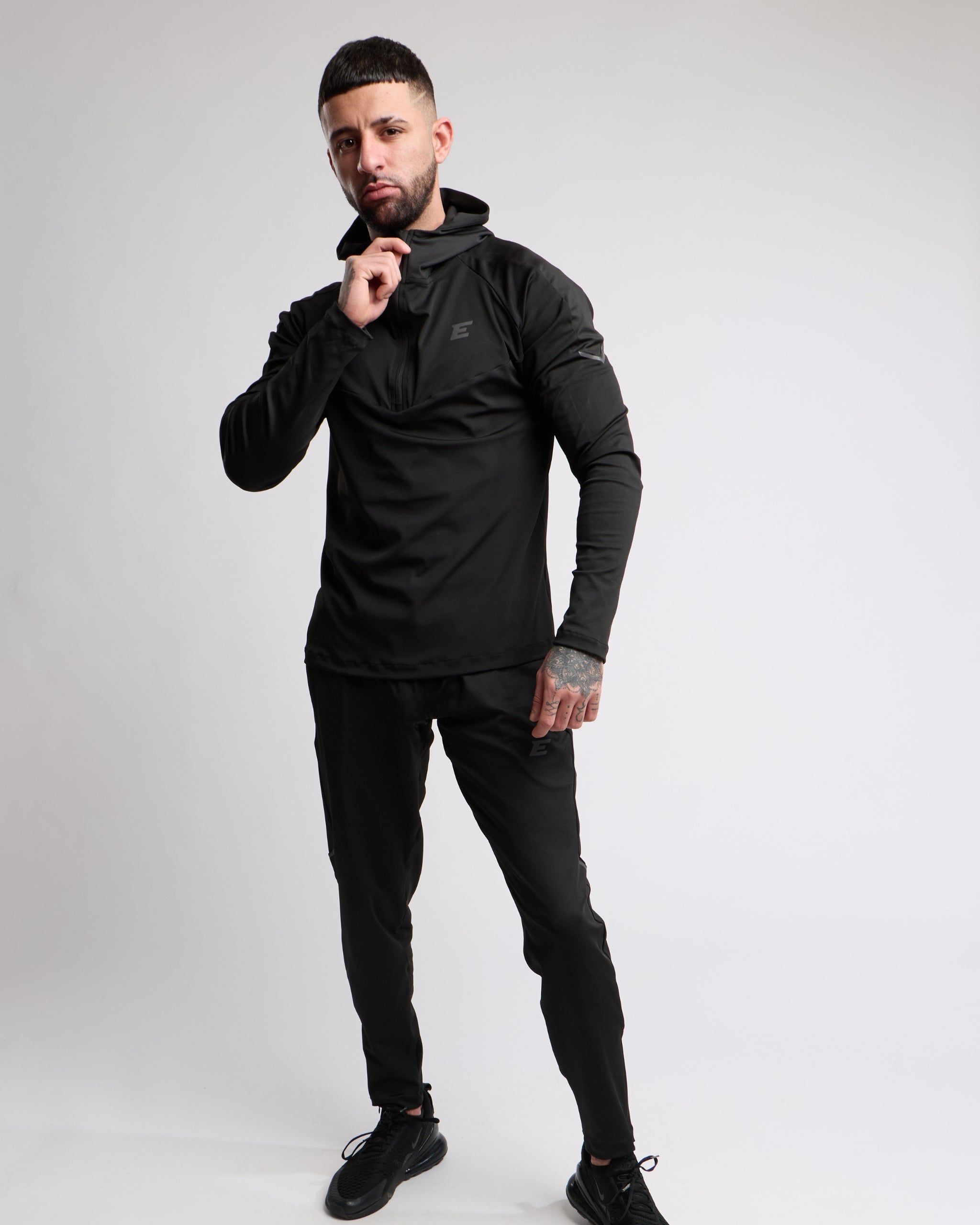 Man wearing a black athletic zip top and bottoms set with elegante brand logo on a white background