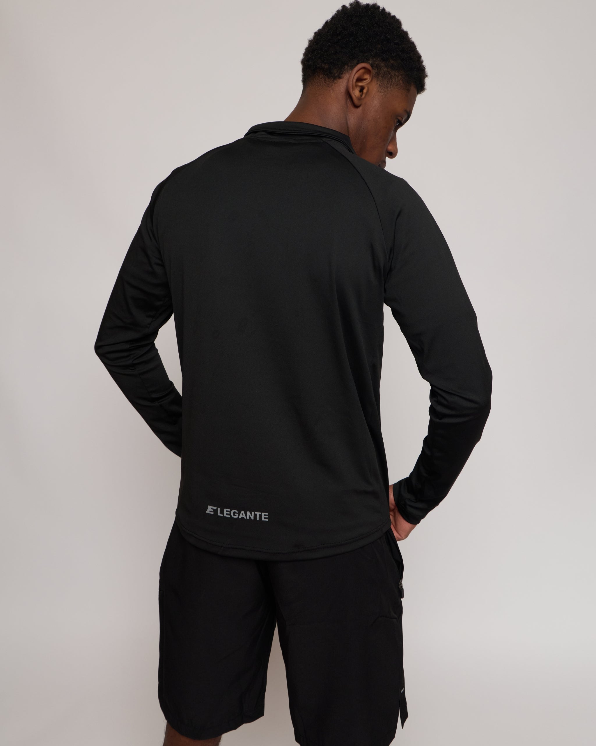 Man wearing a long sleeve black athletic quarter zip top with a white 'E' logo with matching shorts on a light background