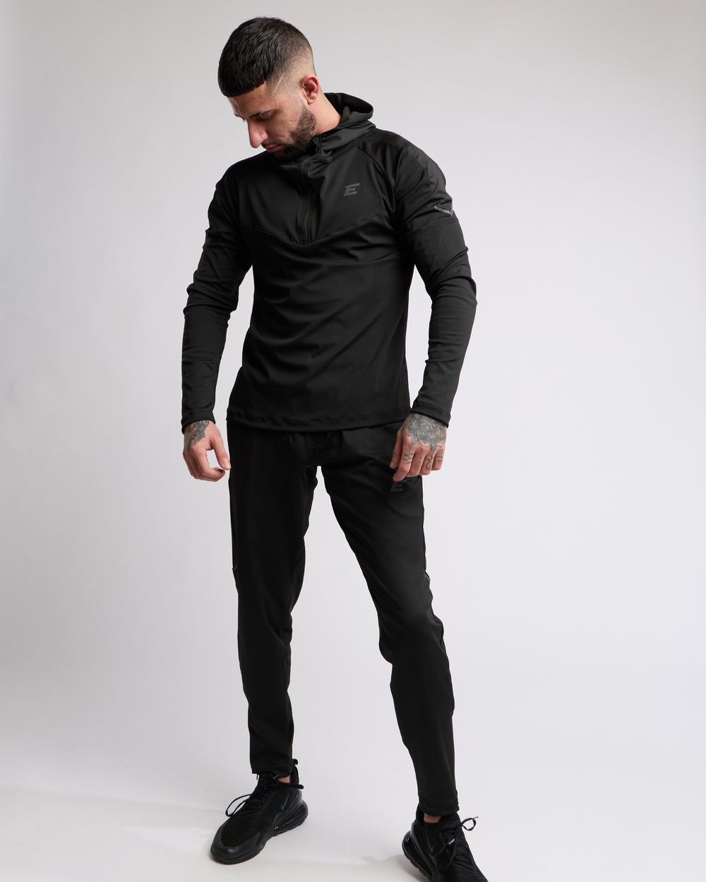 Man wearing a black athletic zip top and bottoms set with elegante brand logo on a white background