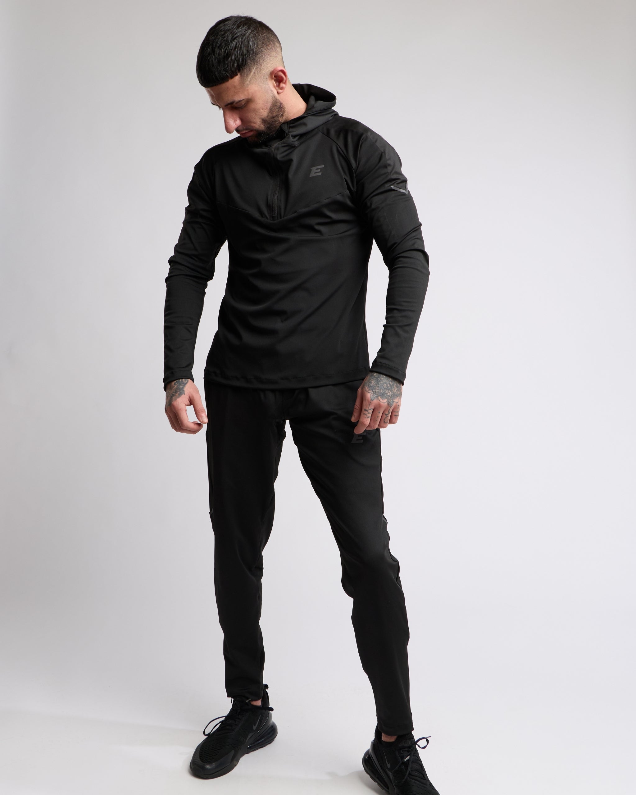 Man wearing a black athletic zip top and bottoms set with elegante brand logo on a white background