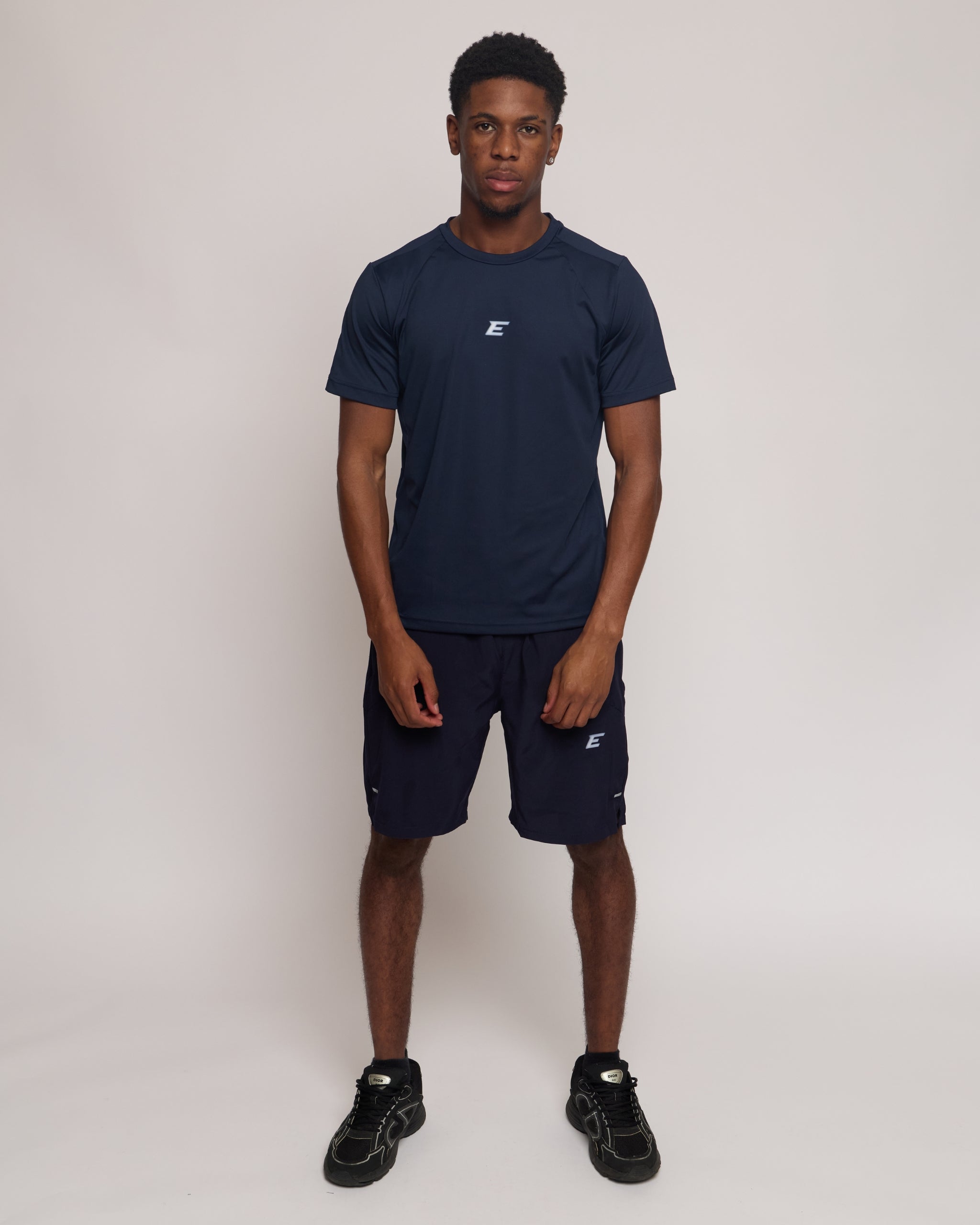 Man wearing a navy athletic shorts and t-shirt outfit with a white 'E' brand logo on white background