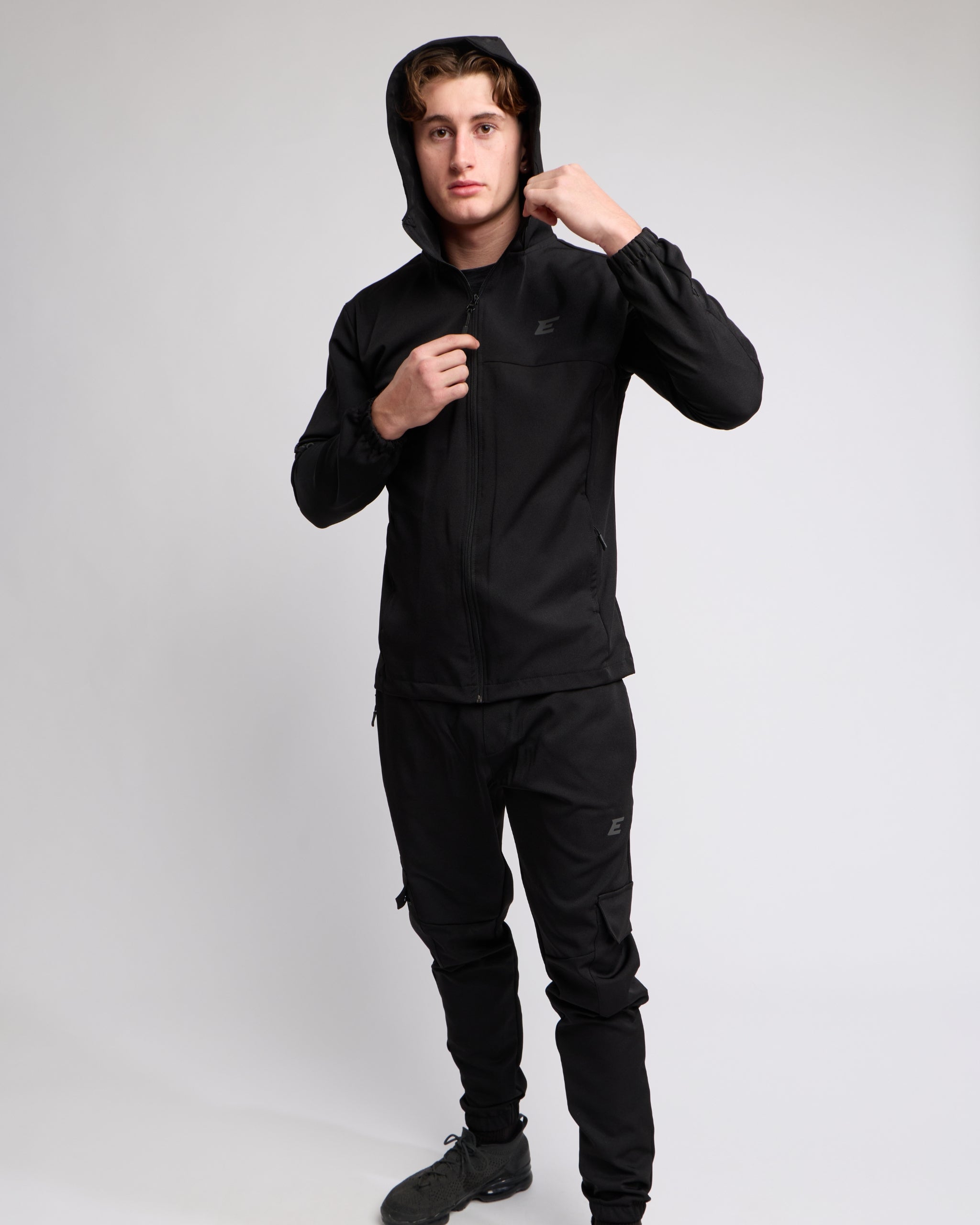 man wearing a black tracksuit set with hood up on a white background