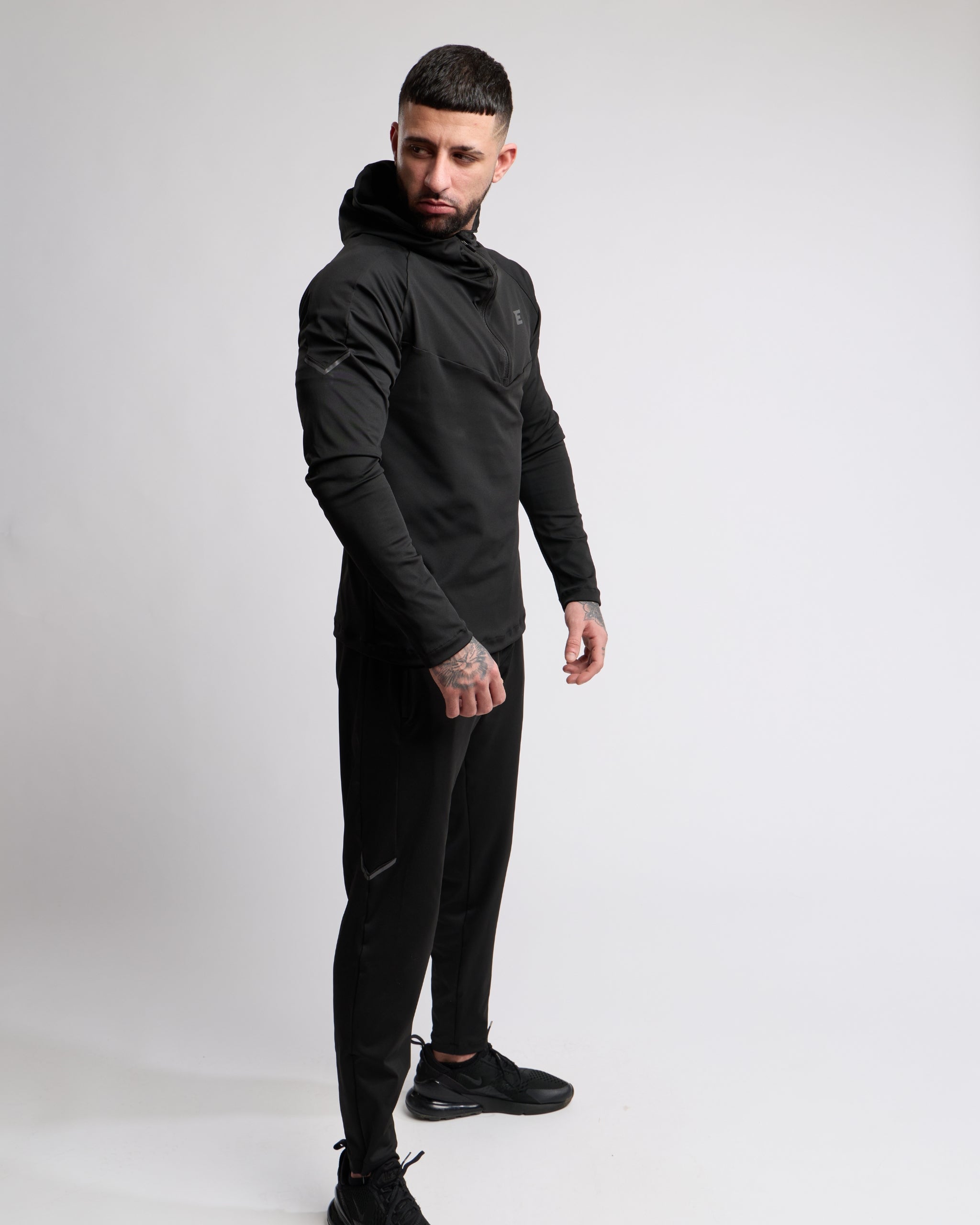 Man wearing a black athletic zip top and bottoms set with elegante brand logo on a white background