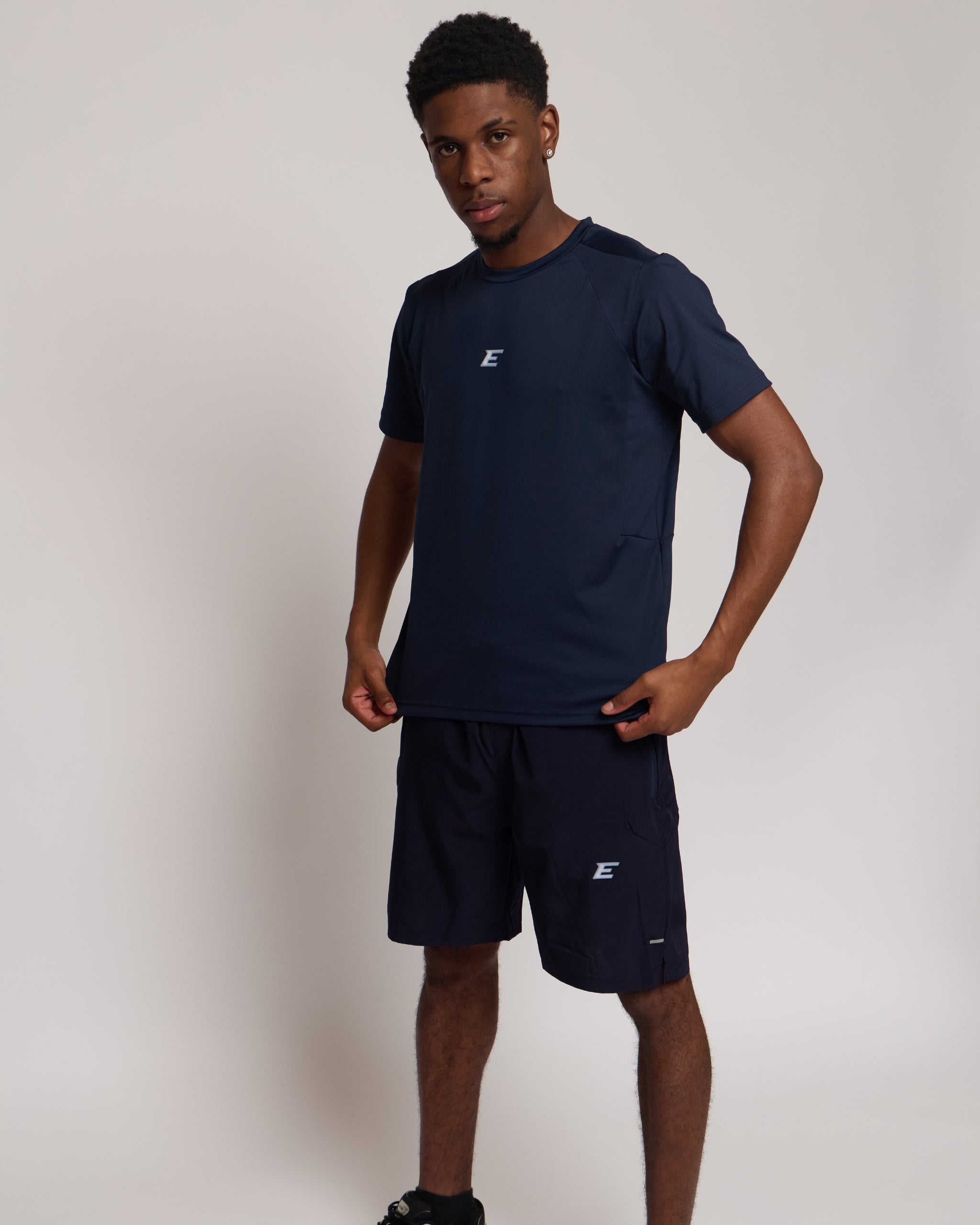Man wearing a navy athletic shorts and t-shirt outfit with a white 'E' brand logo on white background