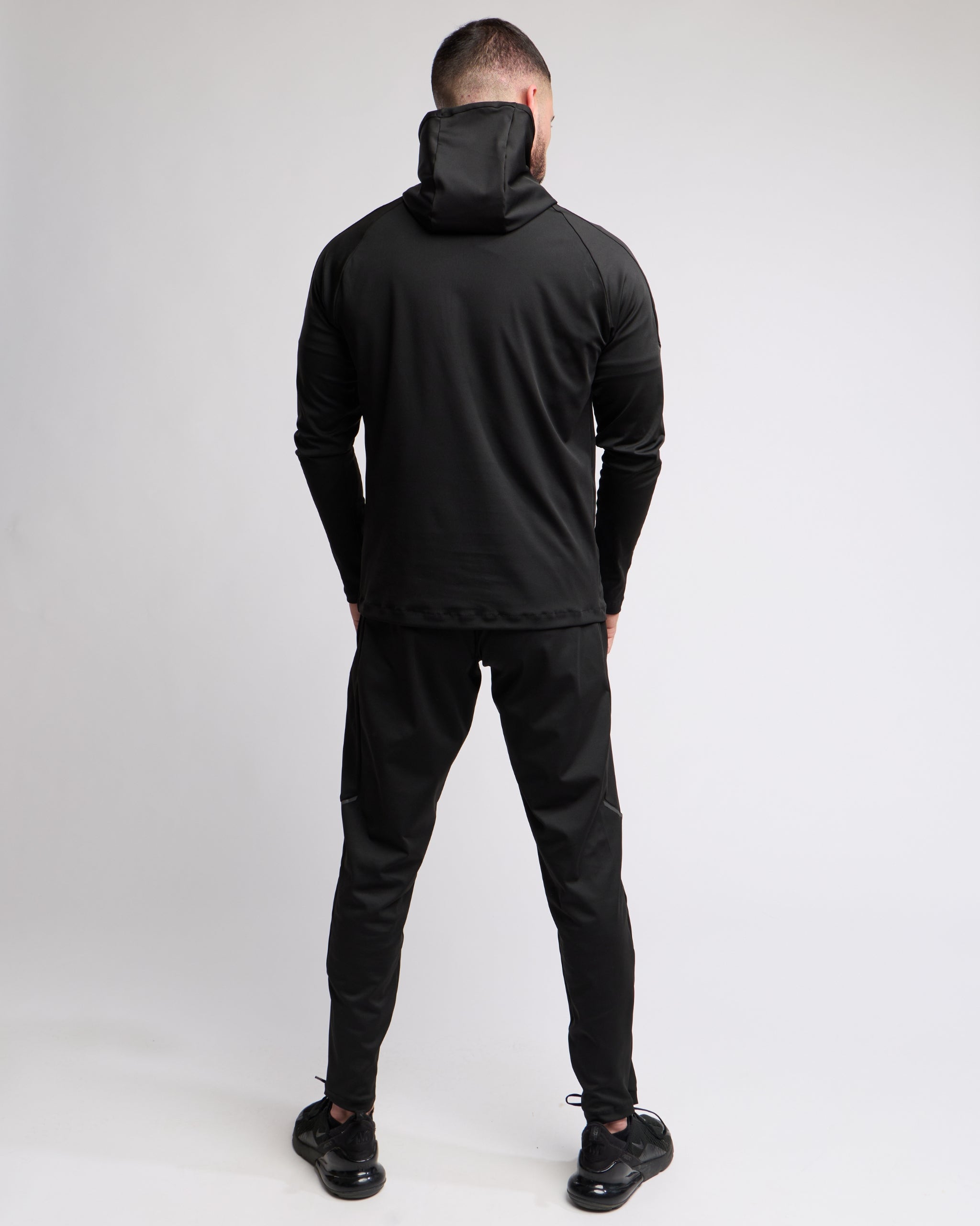 Man wearing a black athletic zip top with hood and bottoms set with elegante brand logo on a white background