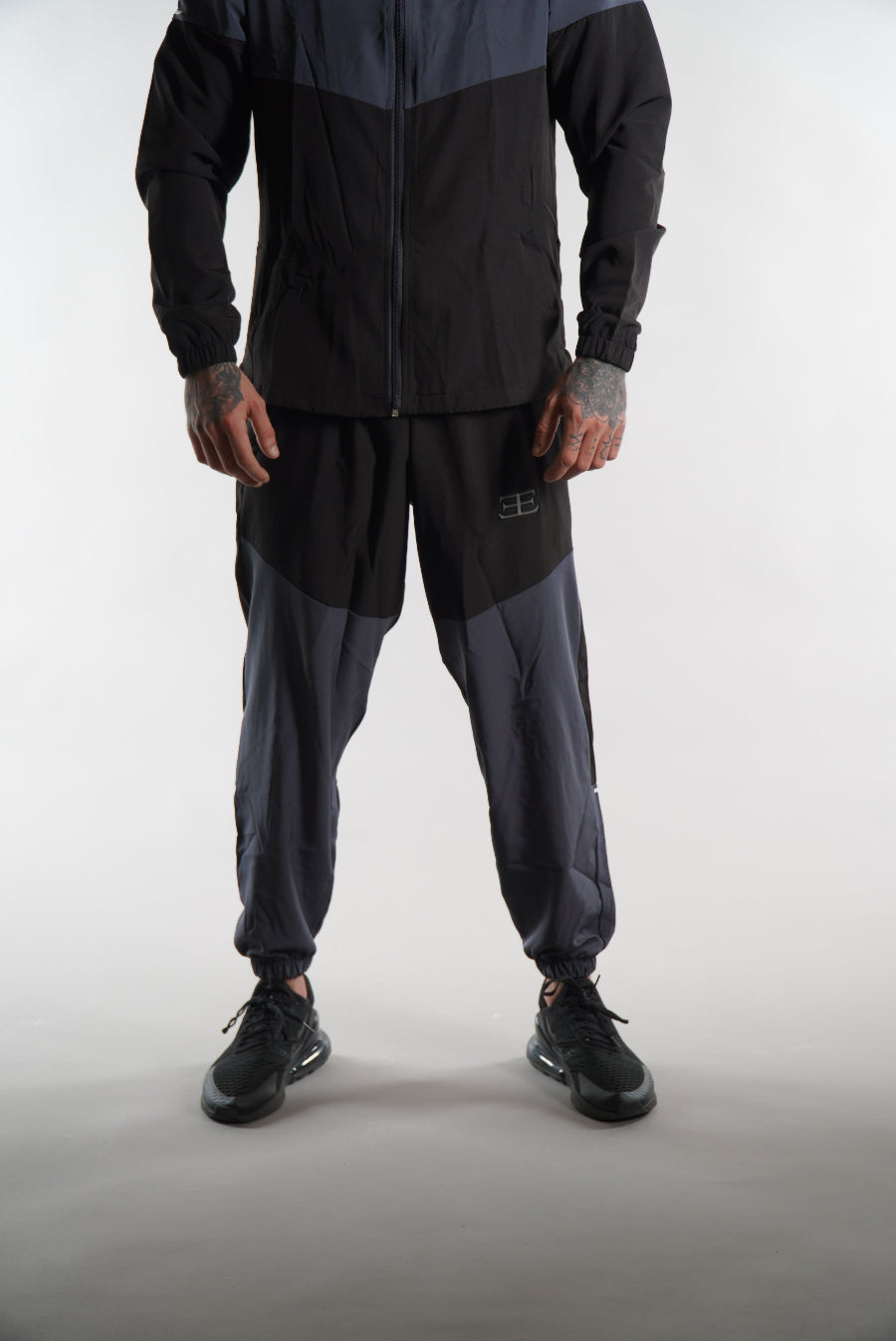 Man wearing black and dark grey tracksuit pants set, on white background, sports clothing for men