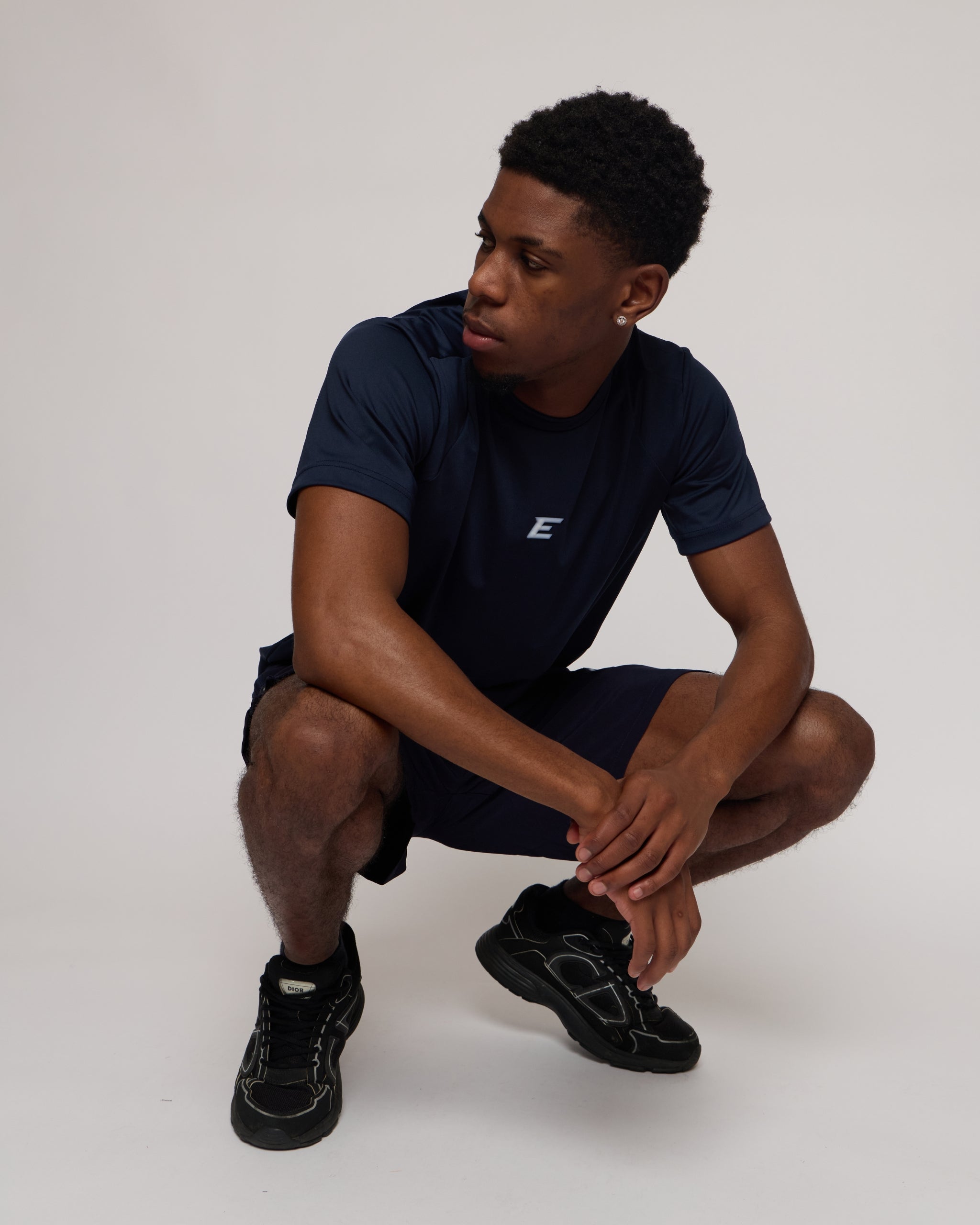 Man wearing a navy athletic shorts and t-shirt outfit with a white 'E' brand logo on white background
