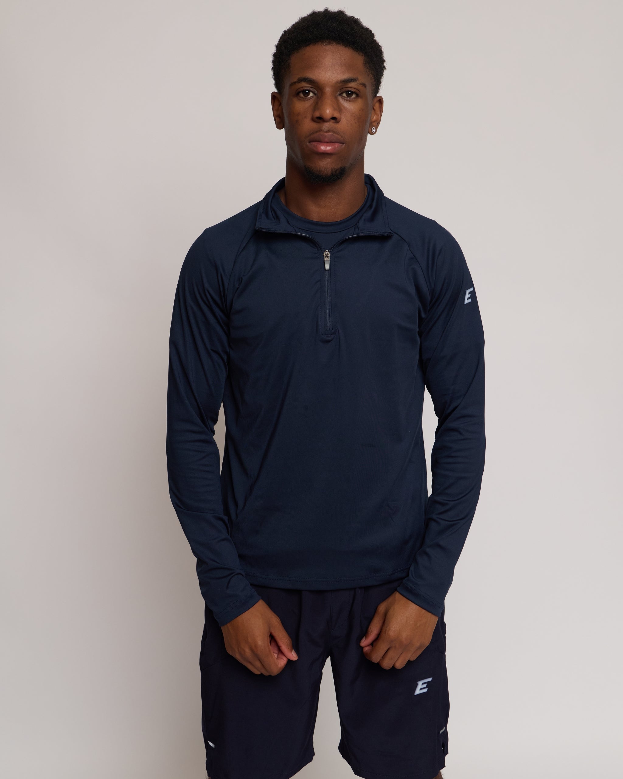 Man wearing a long sleeve navy athletic quarter zip top with a white 'E' logo with matching shorts on a light background