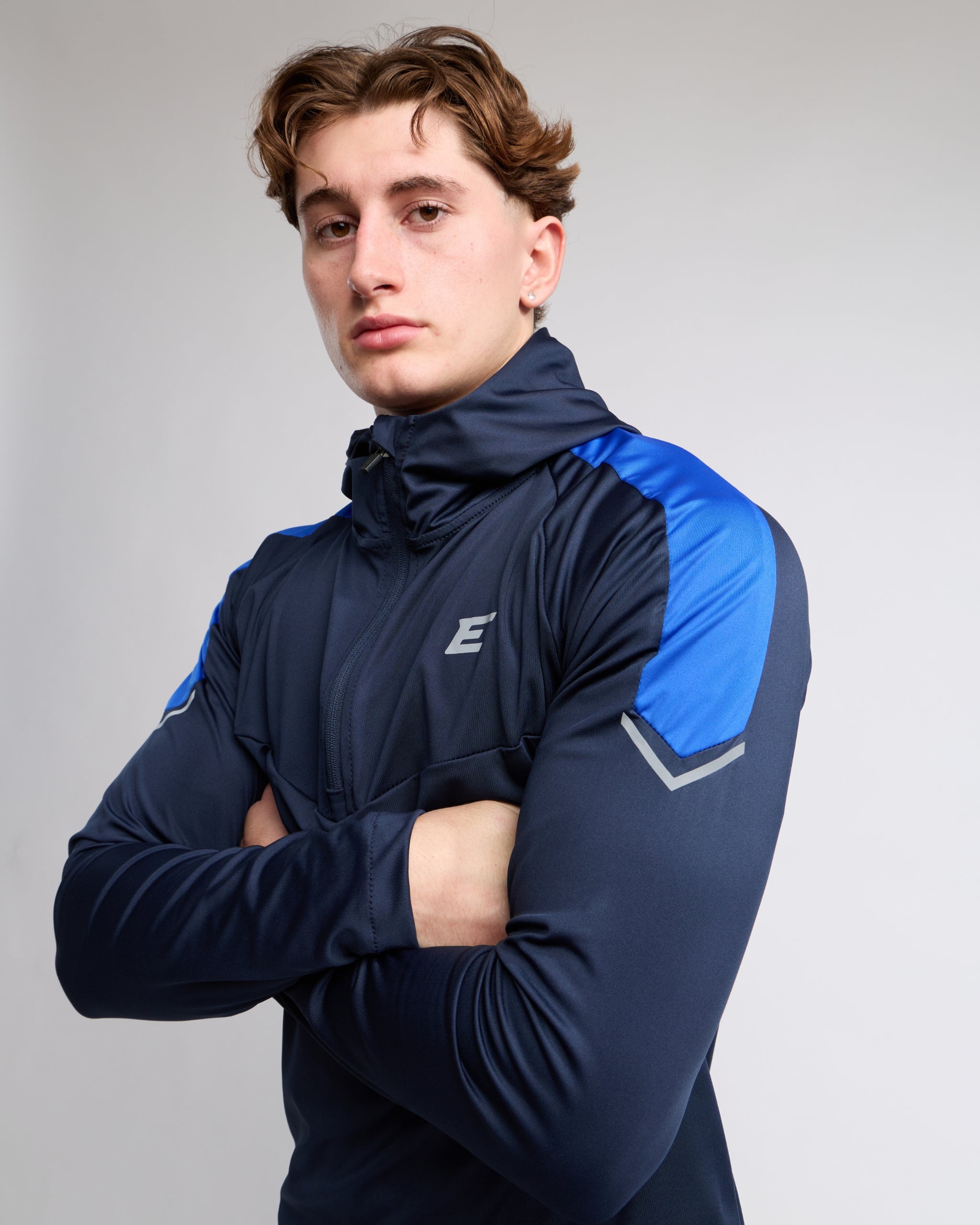 Man wearing a navy and blue athletic zip top with an E logo on a gray background