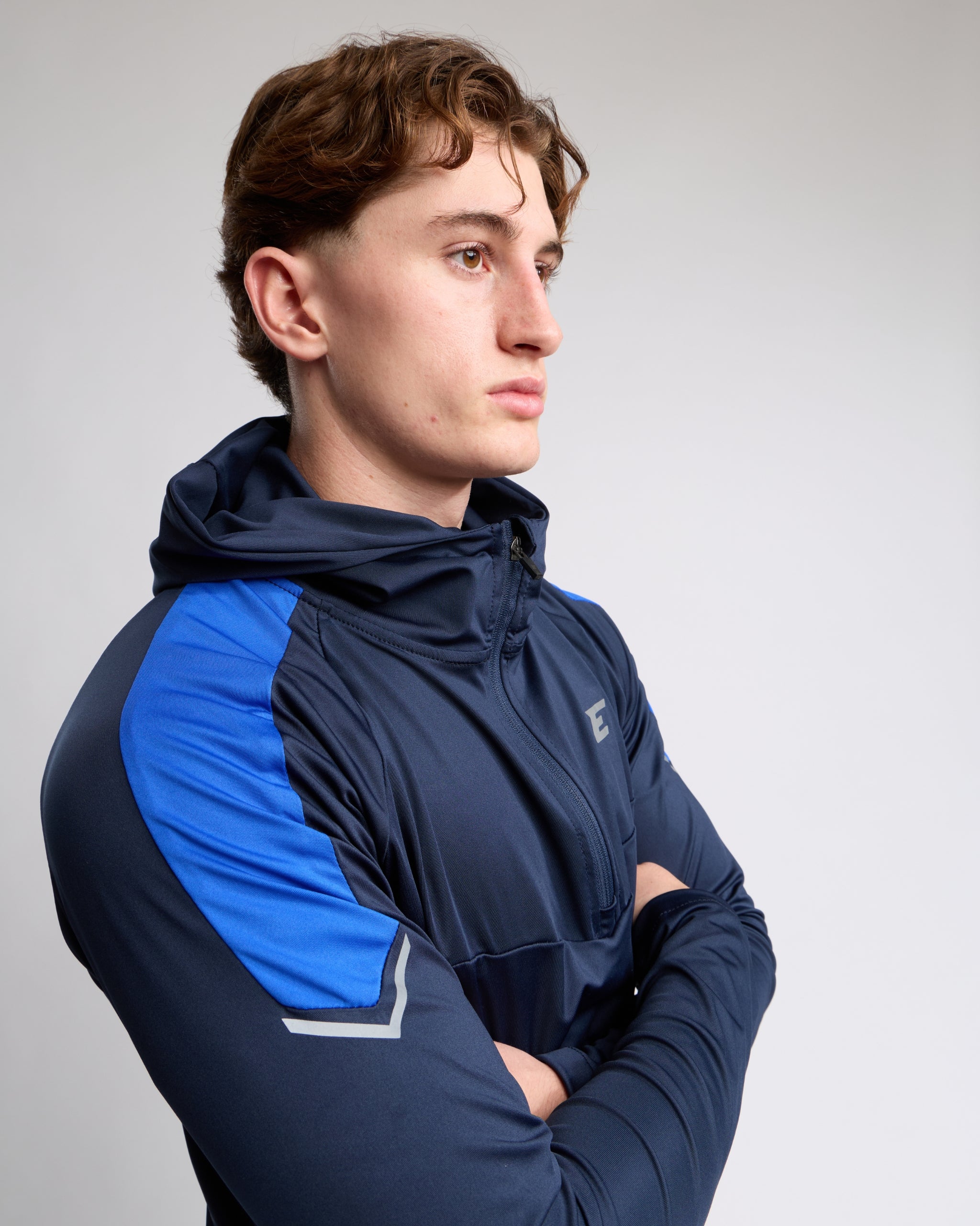 Man wearing a navy and blue athletic zip top with an E logo on a gray background