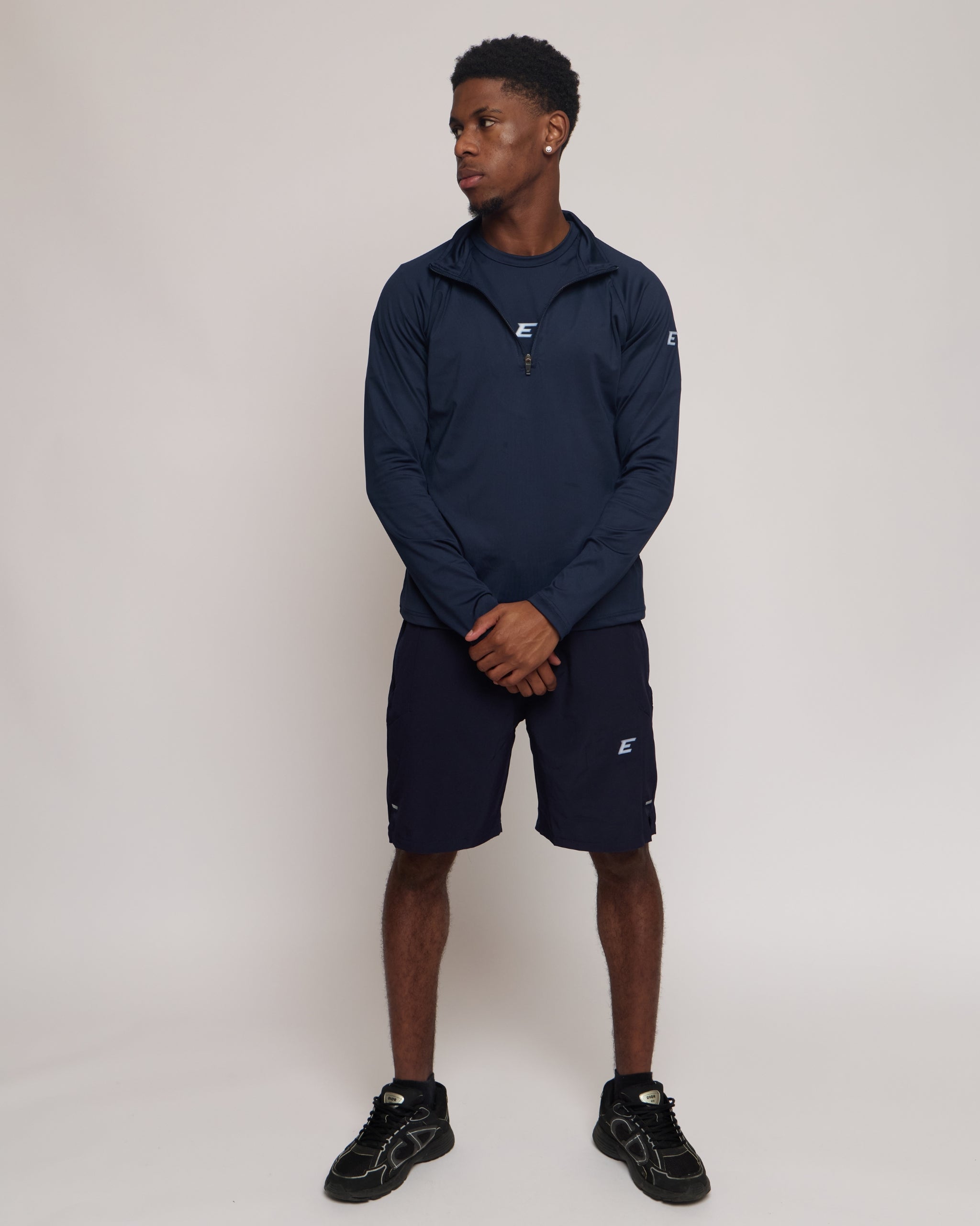 Man wearing a long sleeve navy athletic quarter zip top with a white 'E' logo with matching shorts on a light background