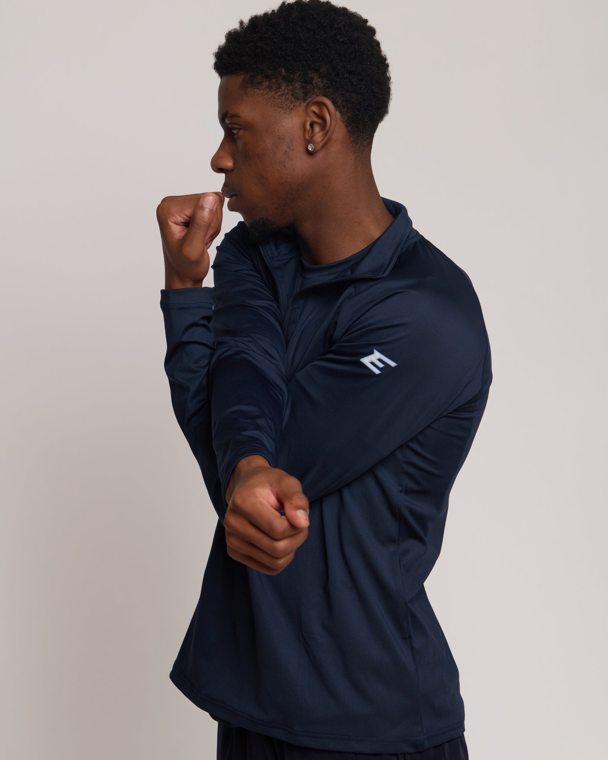 Man wearing a long sleeve navy athletic quarter zip top with a white 'E' logo with matching shorts on a light background
