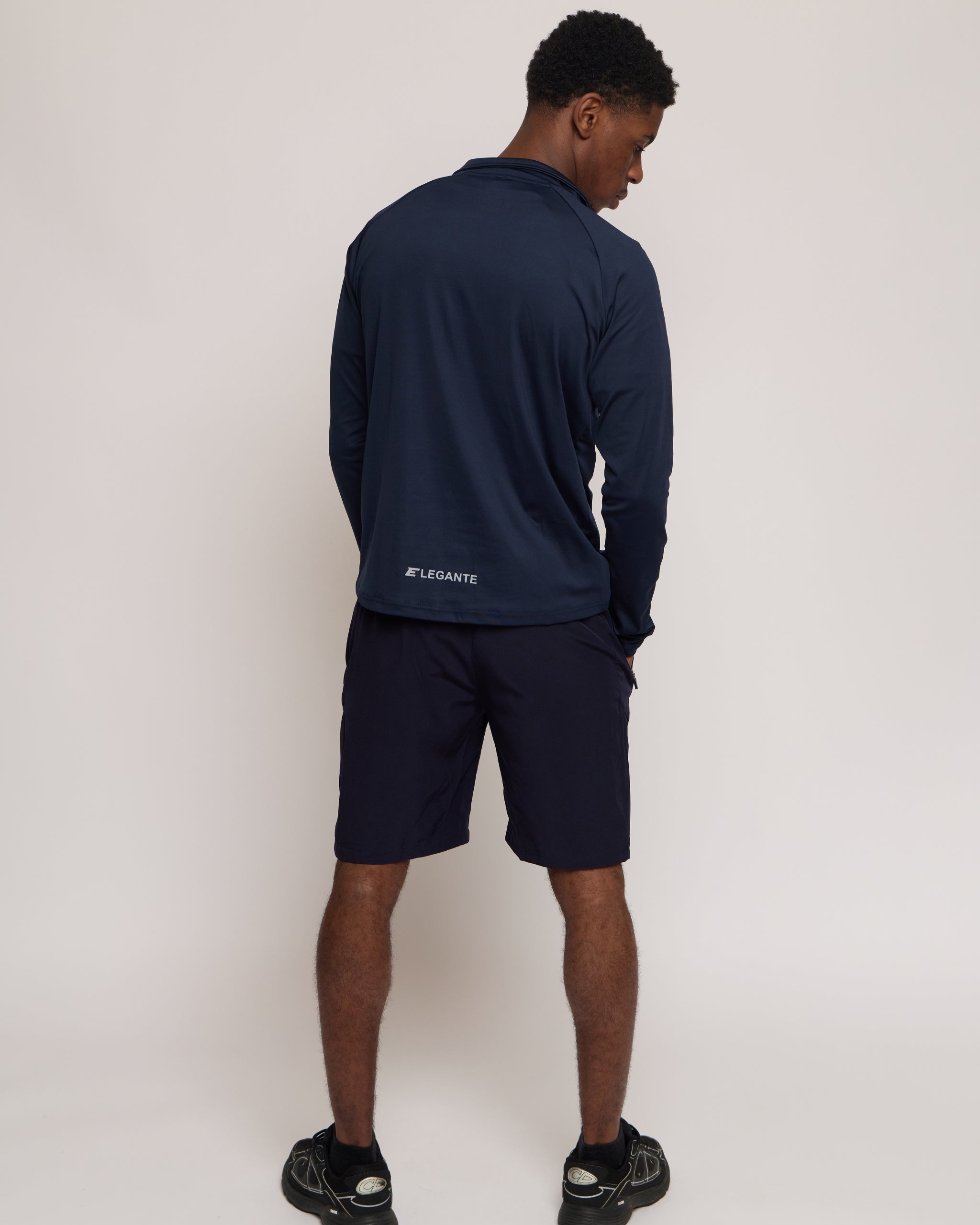 man wearing a navy long-sleeve zip top and shorts with an elegante brand logo on a white background