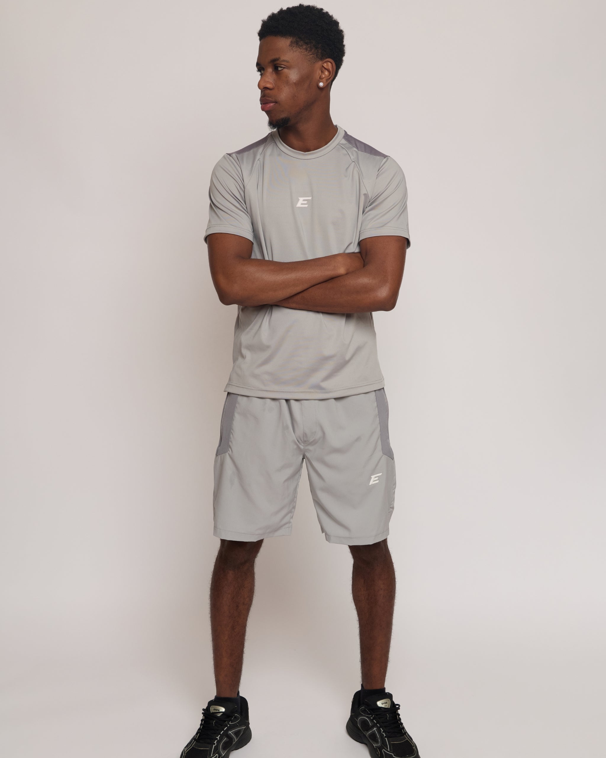 Man wearing a gray athletic shorts and t-shirt outfit with an 'E' logo on a grey background