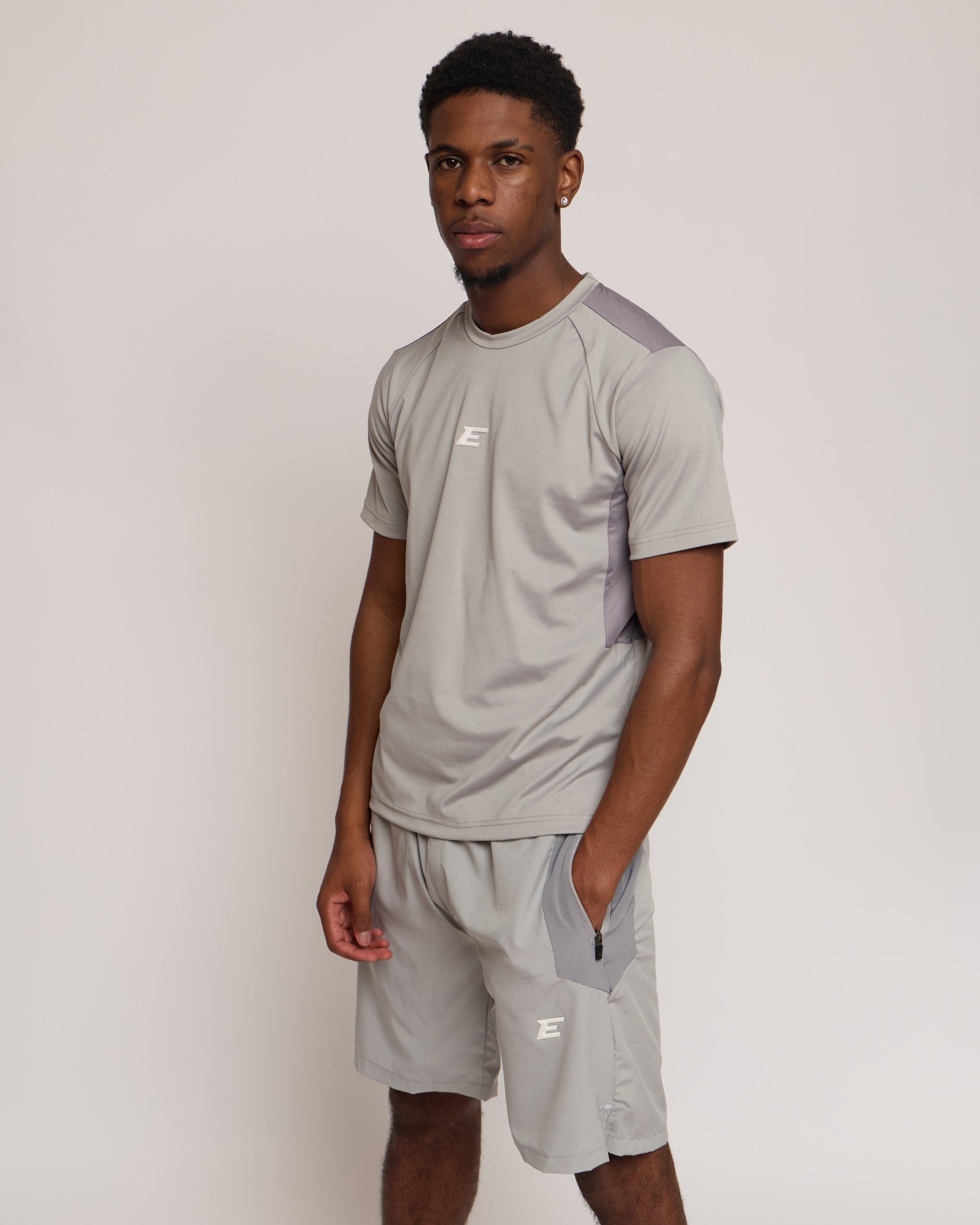 Man wearing a gray athletic shorts and t-shirt outfit with an 'E' logo on a grey background