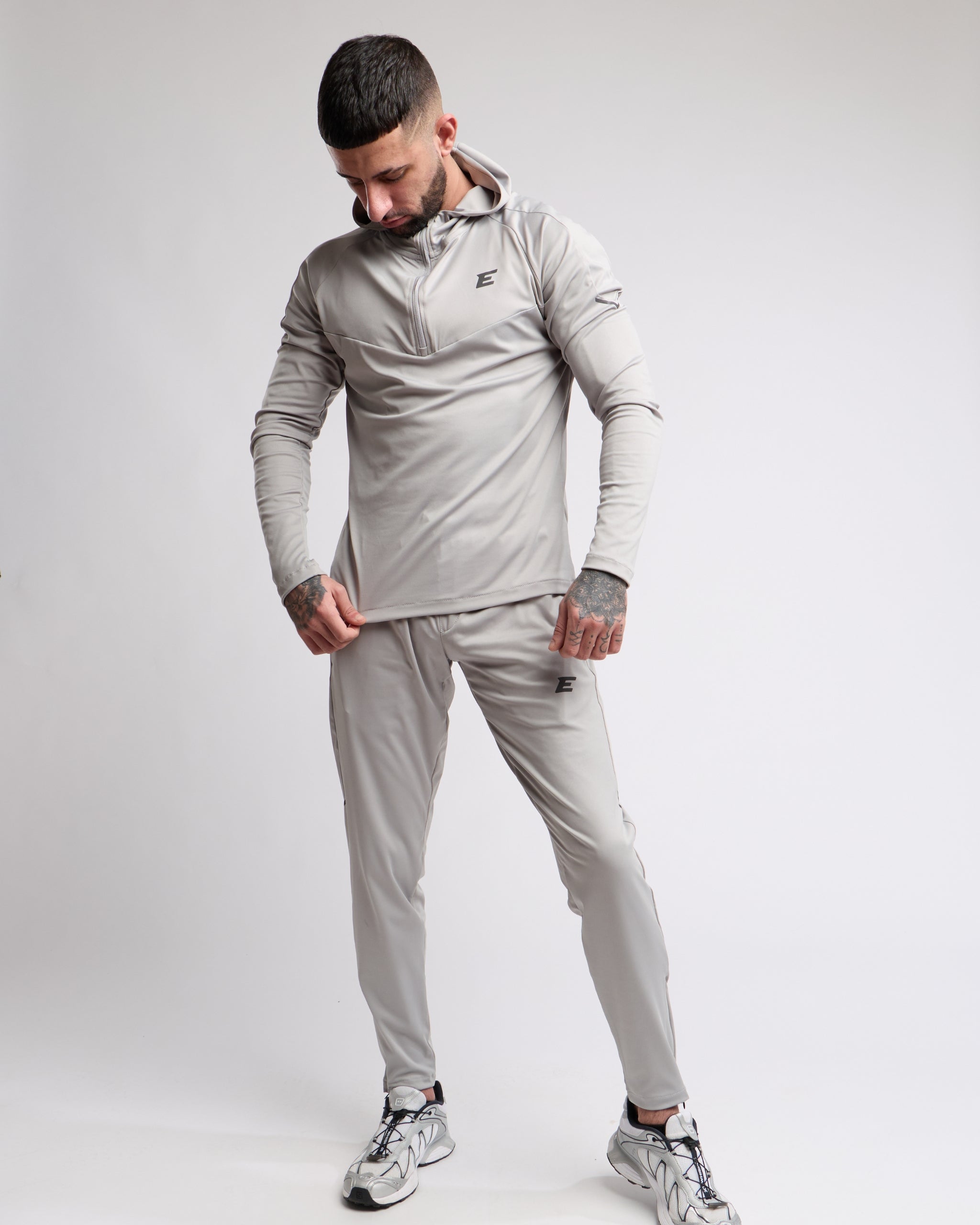 Man wearing a light gray tracksuit with a brand logo on a white background