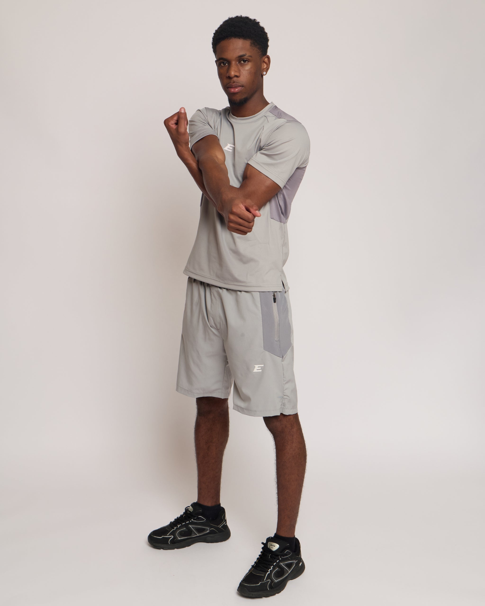 Man wearing a gray athletic shorts and t-shirt outfit with an 'E' logo on a grey background