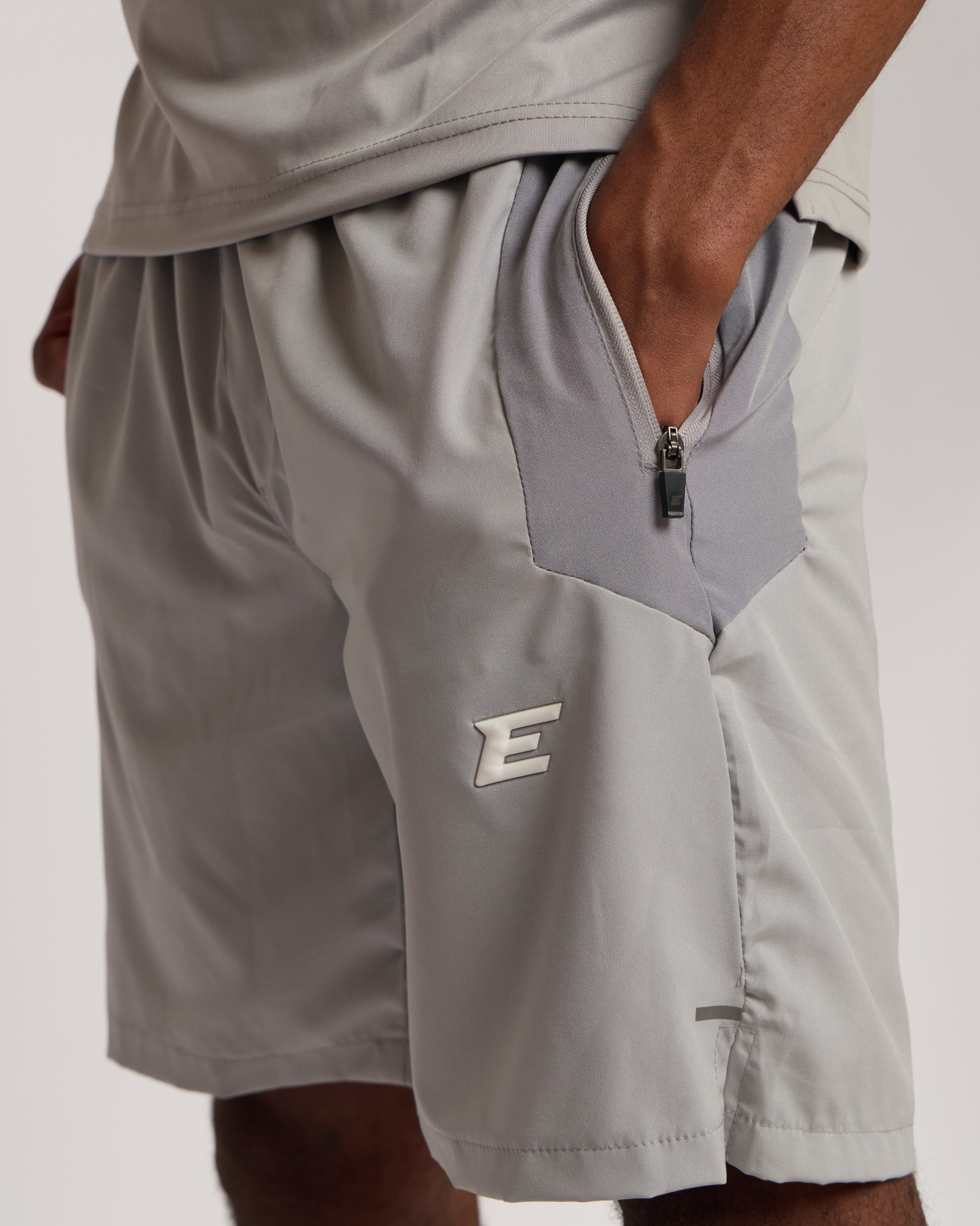 Man wearing a gray athletic shorts and t-shirt outfit with an 'E' logo on a grey background