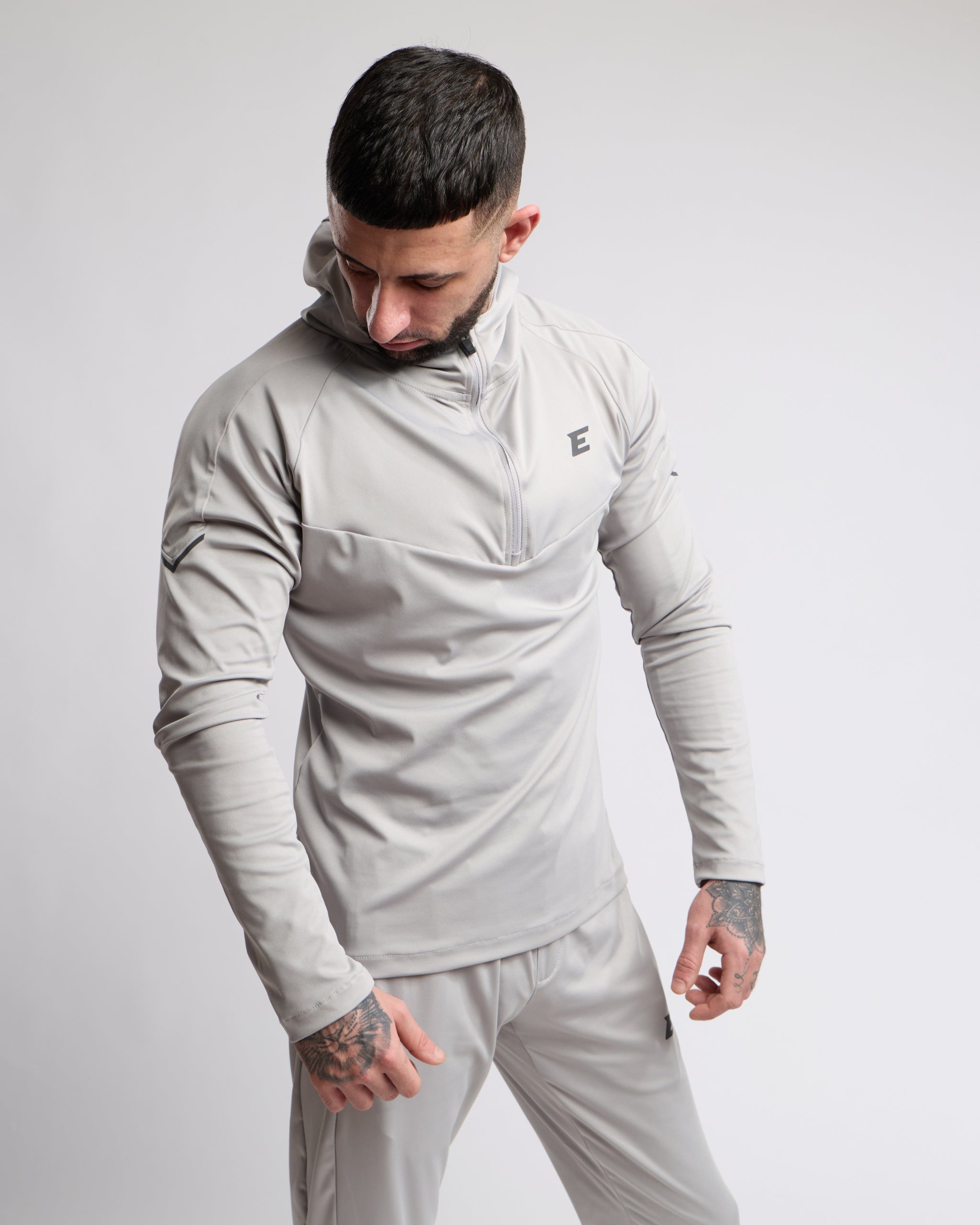 Man wearing a light gray athletic outfit with a brand logo on a plain background