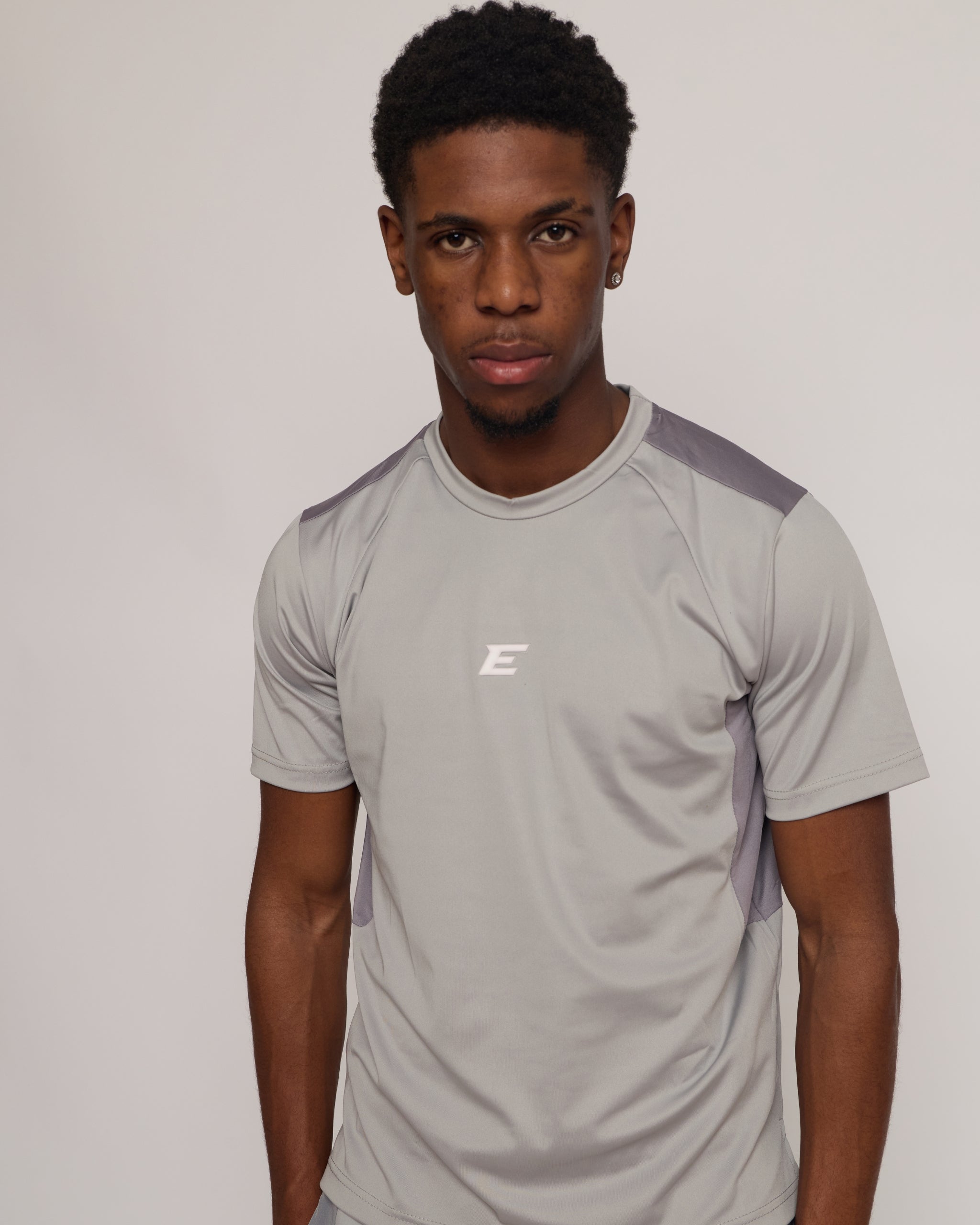 man wearing a gray athletic shirt with an elegante logo on a plain background