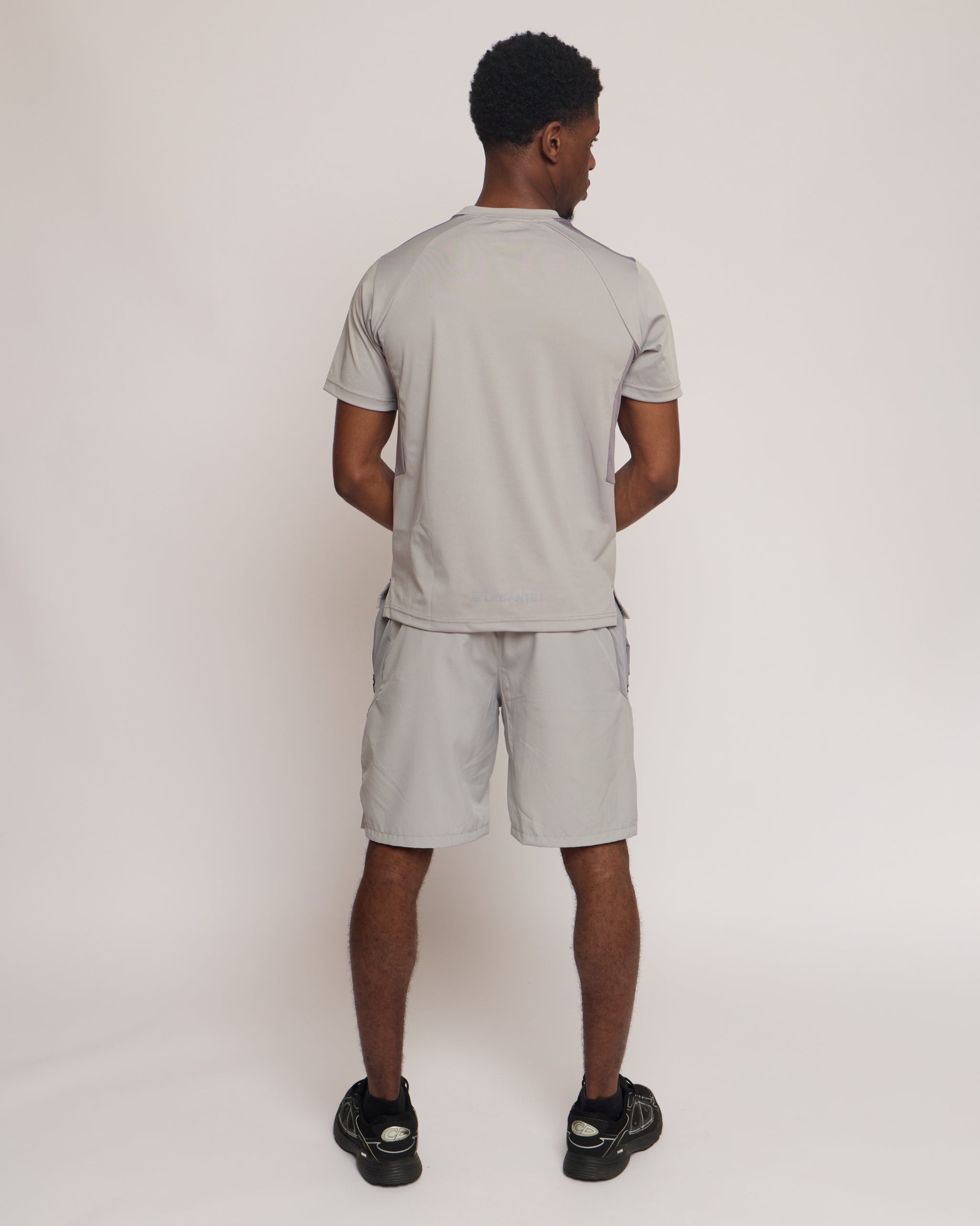 Man wearing a gray athletic shorts and t-shirt outfit with an 'E' logo on a grey background