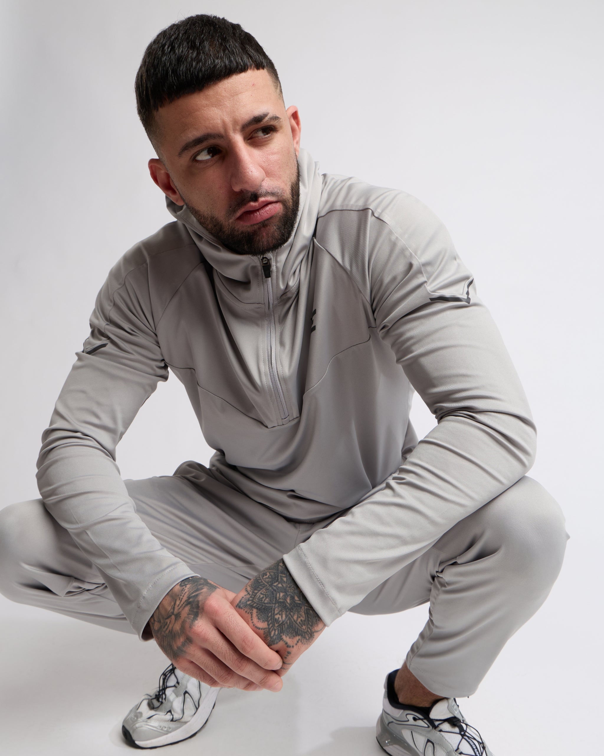Man wearing a gray tracksuit posing on a white background