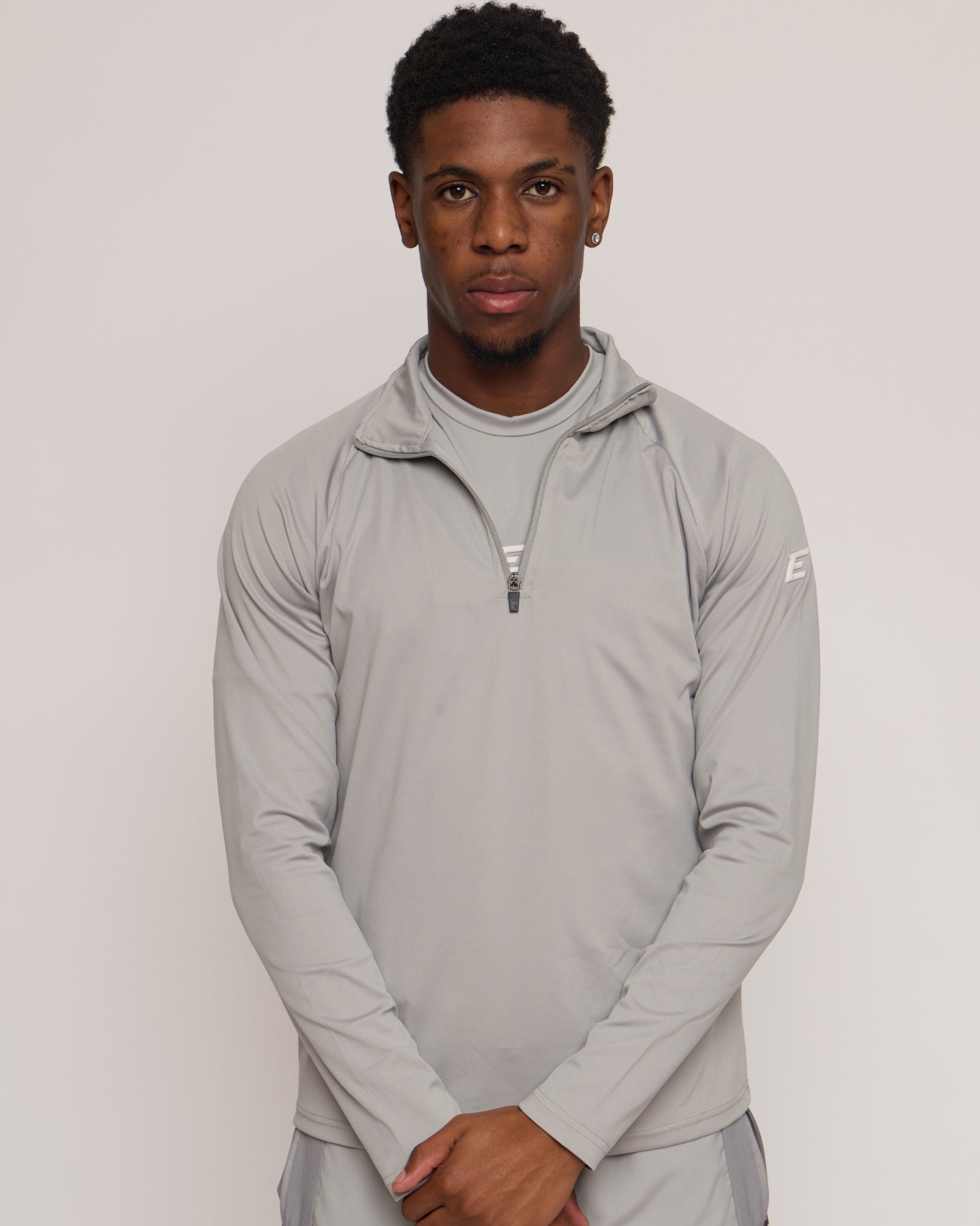 Man wearing a gray athletic quarter zip top with a white 'E' logo on a light background