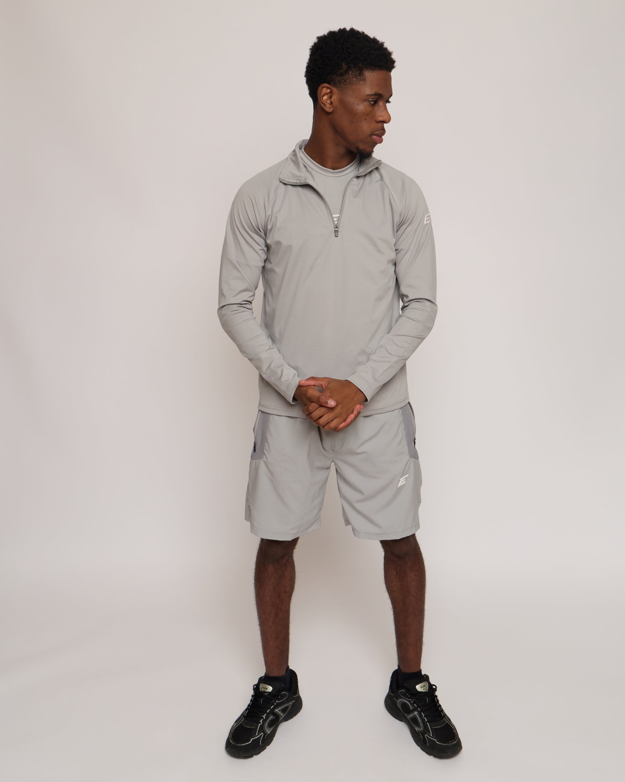 Man wearing a gray athletic quarter zip top with a white 'E' logo on with matching shorts on a light background