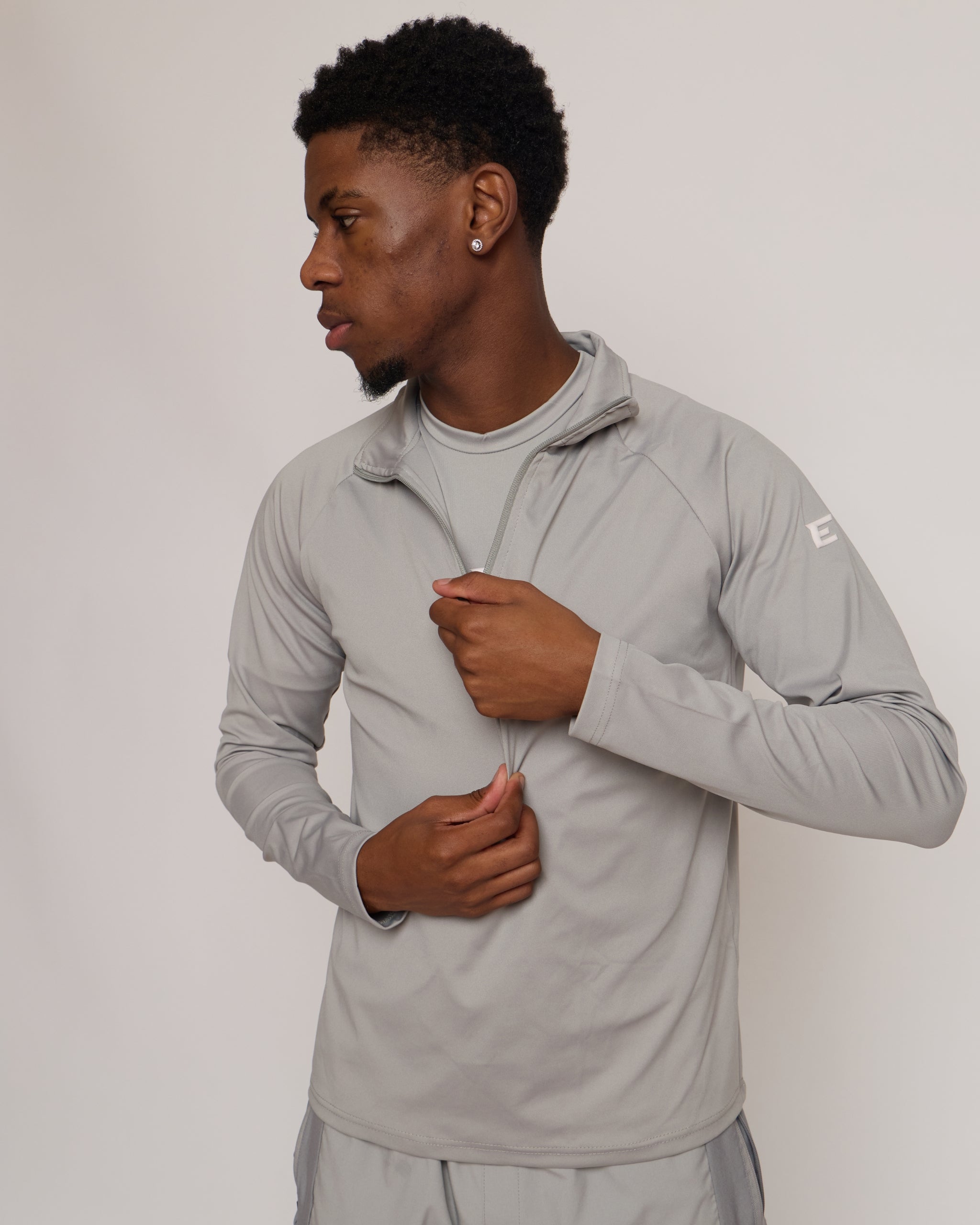 Man wearing a gray athletic quarter zip top with a white 'E' logo on a light background