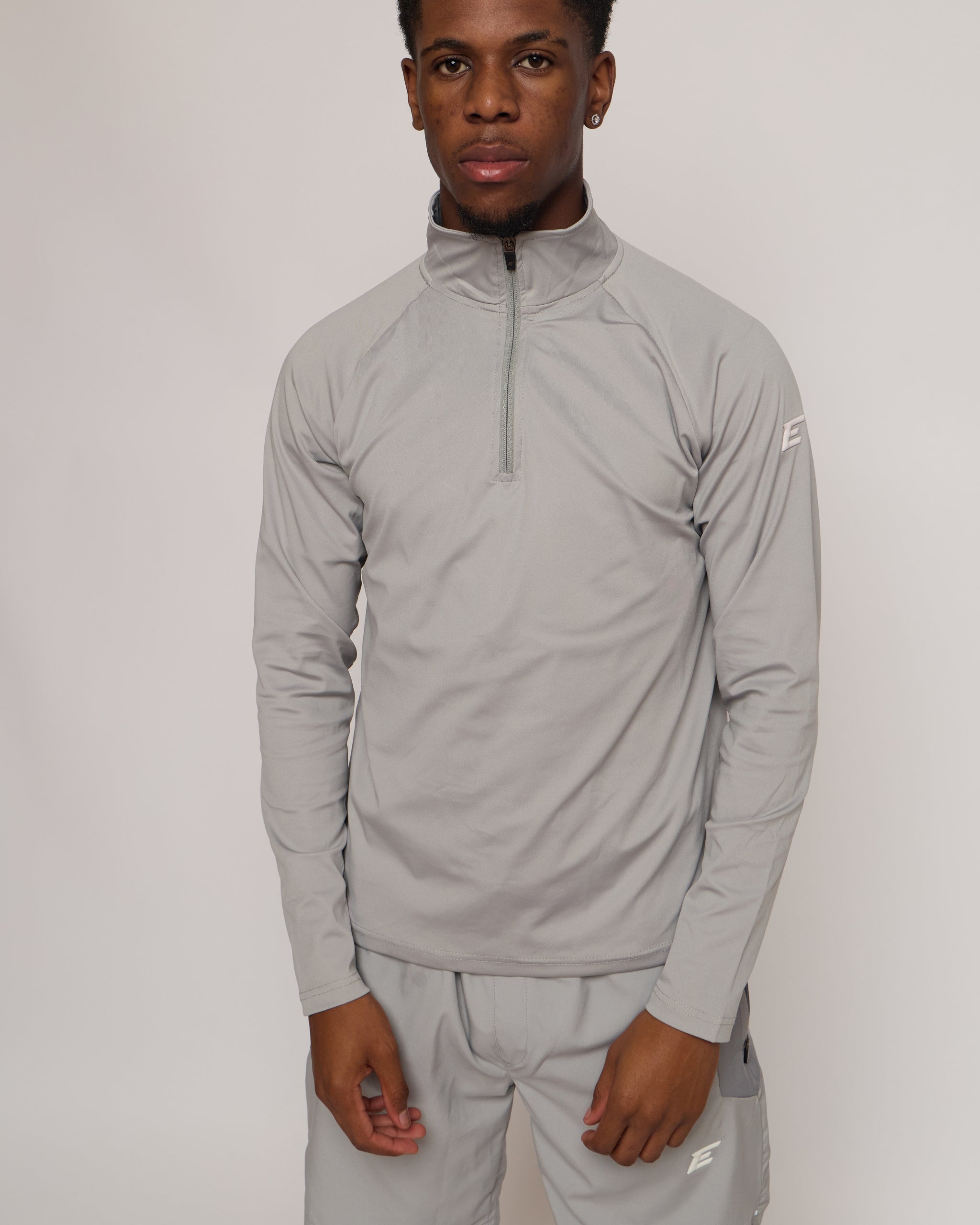 Man wearing a gray athletic quarter zip top with a white 'E' logo on with matching shorts on a light background