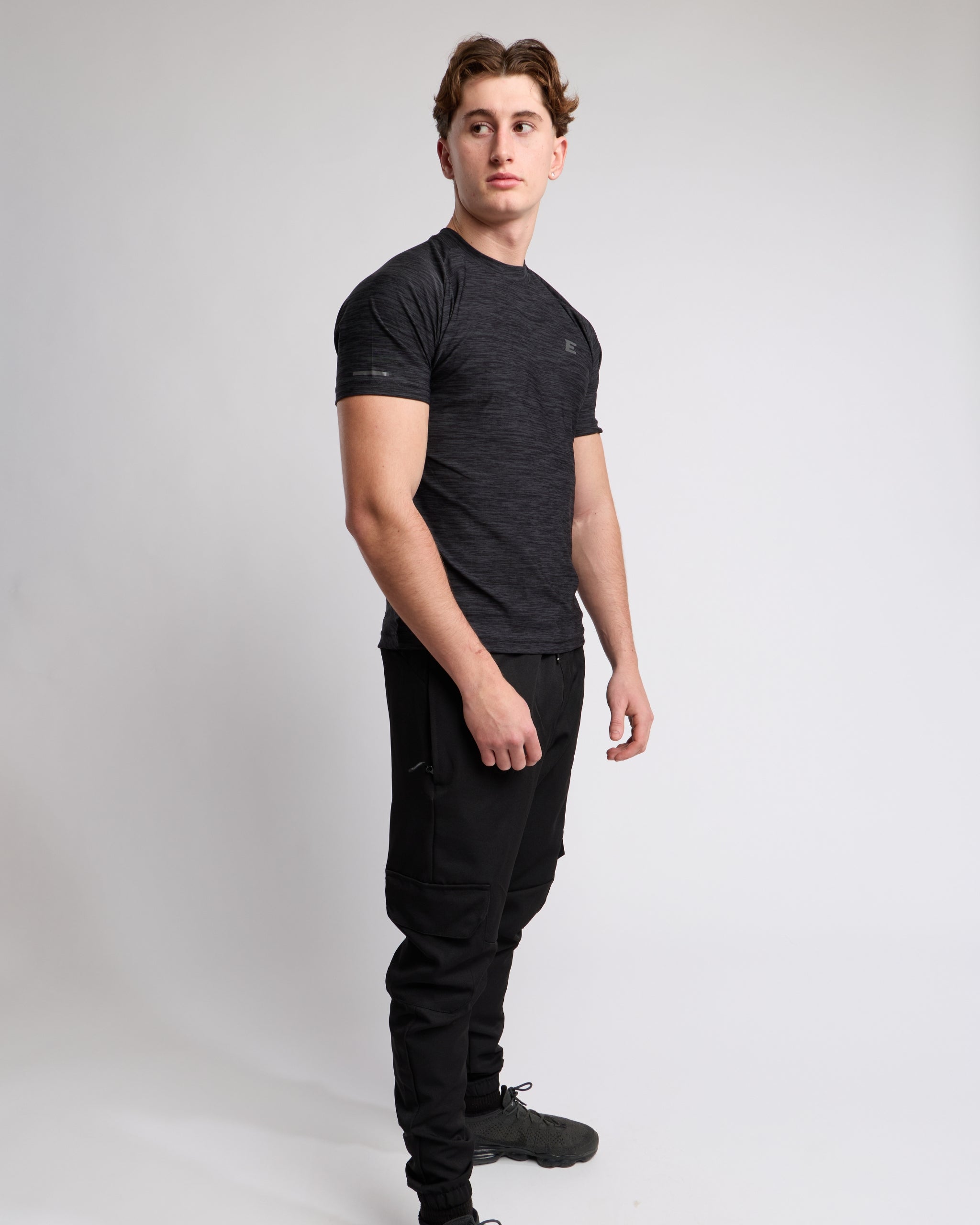 Man wearing a black athletic t-shirt and joggers with a elegante london logo on a light gray background