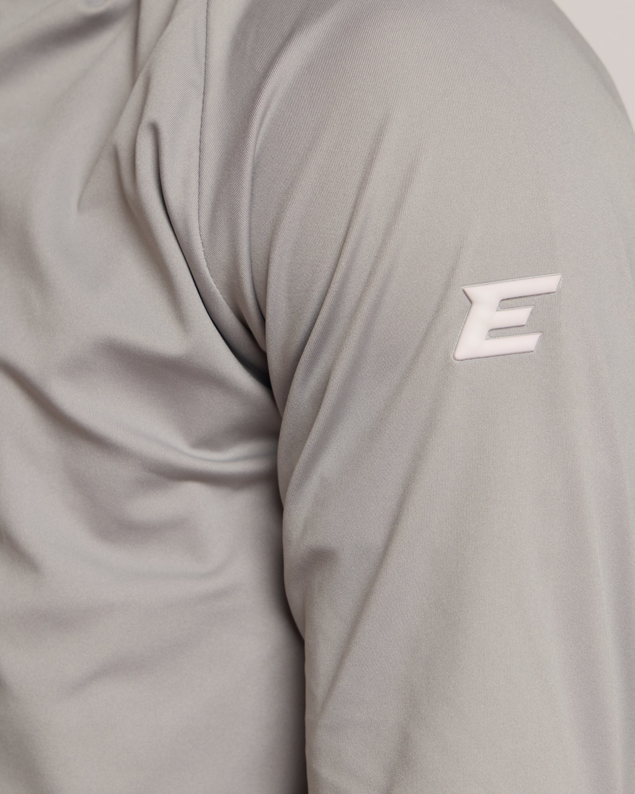 Man wearing a gray athletic quarter zip top with a white 'E' logo on a light background