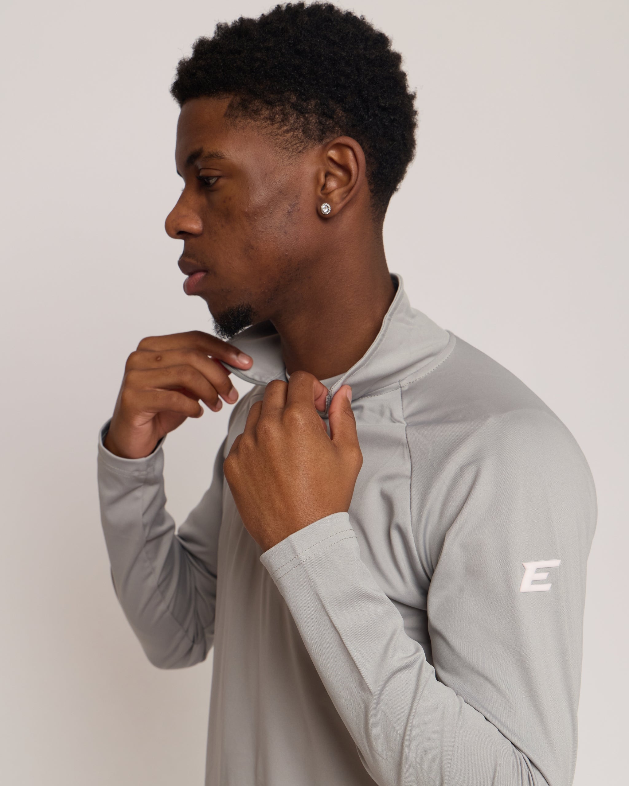 Man wearing a gray athletic quarter zip top with a white 'E' logo on a light background