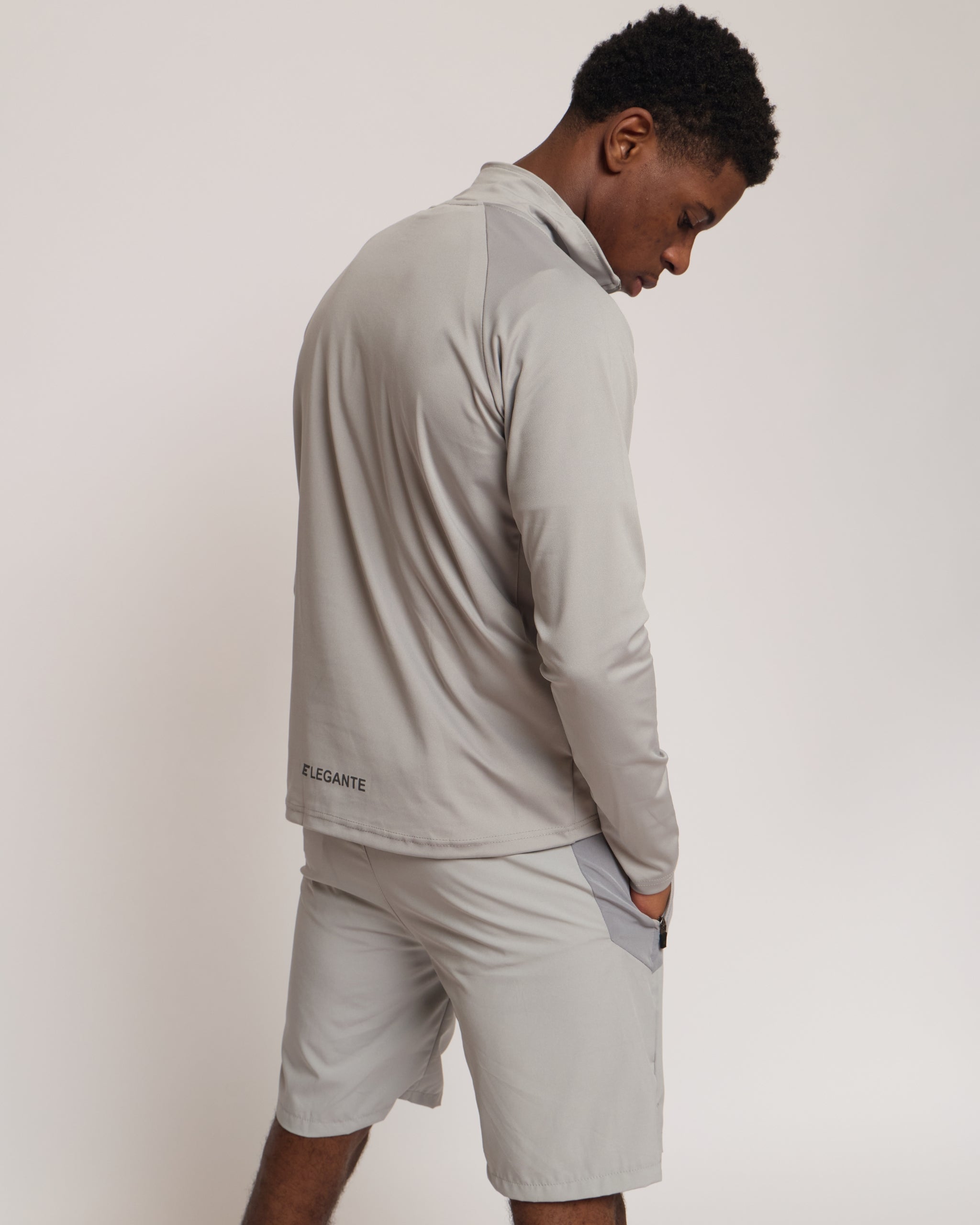 Man wearing a gray athletic quarter zip top with a white 'Elegante' logo on with matching shorts on a light background