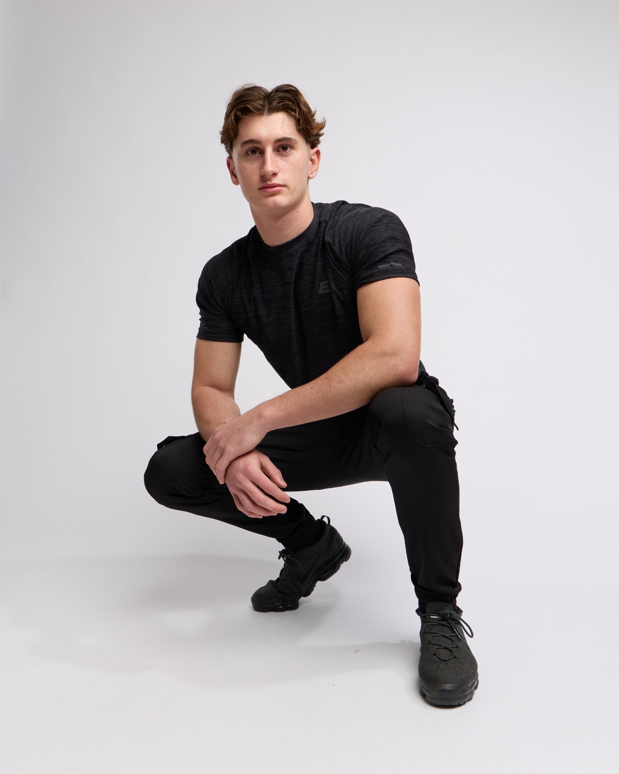 Man wearing a black athletic t-shirt and joggers with a elegante london logo on a light gray background