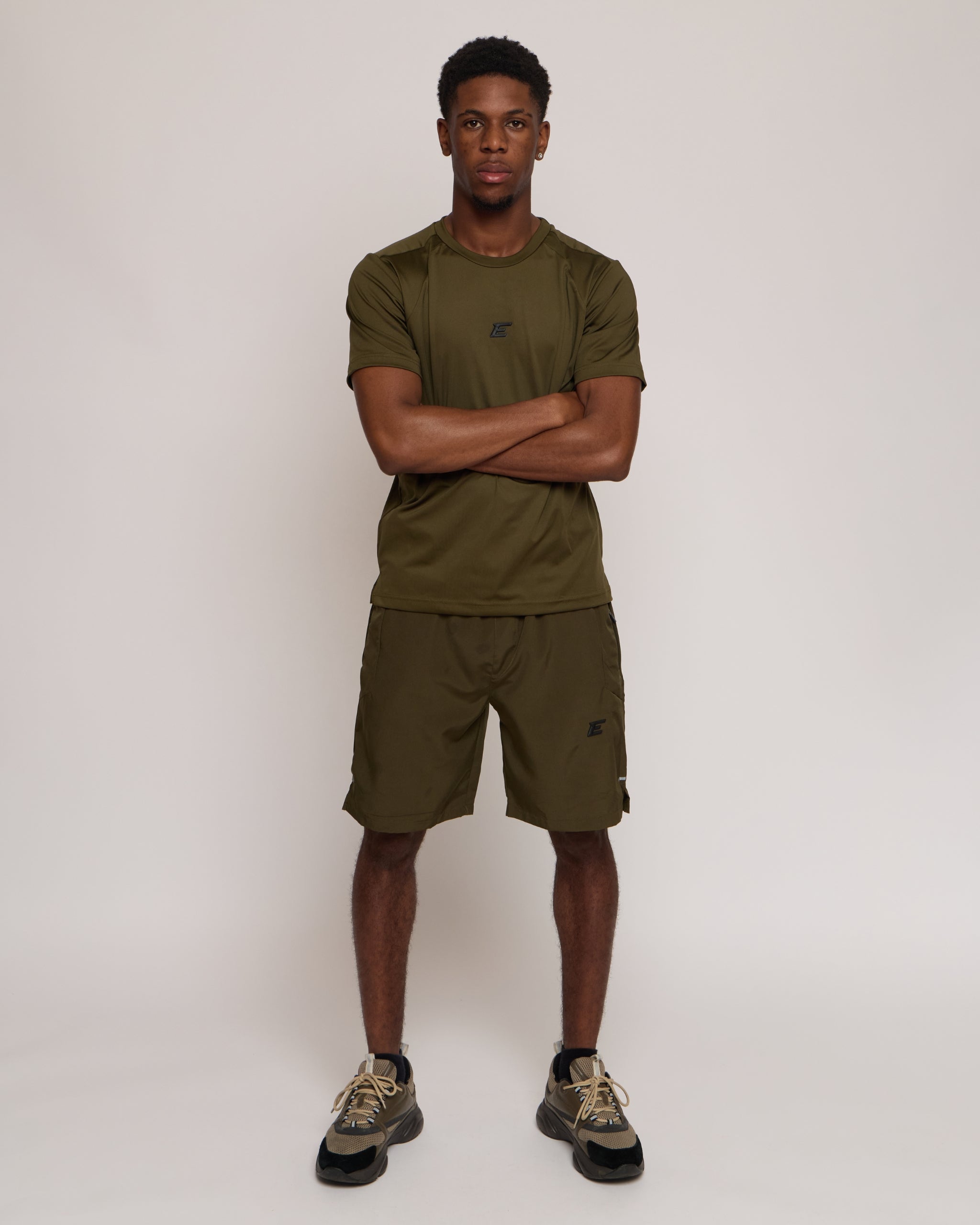 Man wearing a green khaki athletic shorts and t-shirt outfit on white background