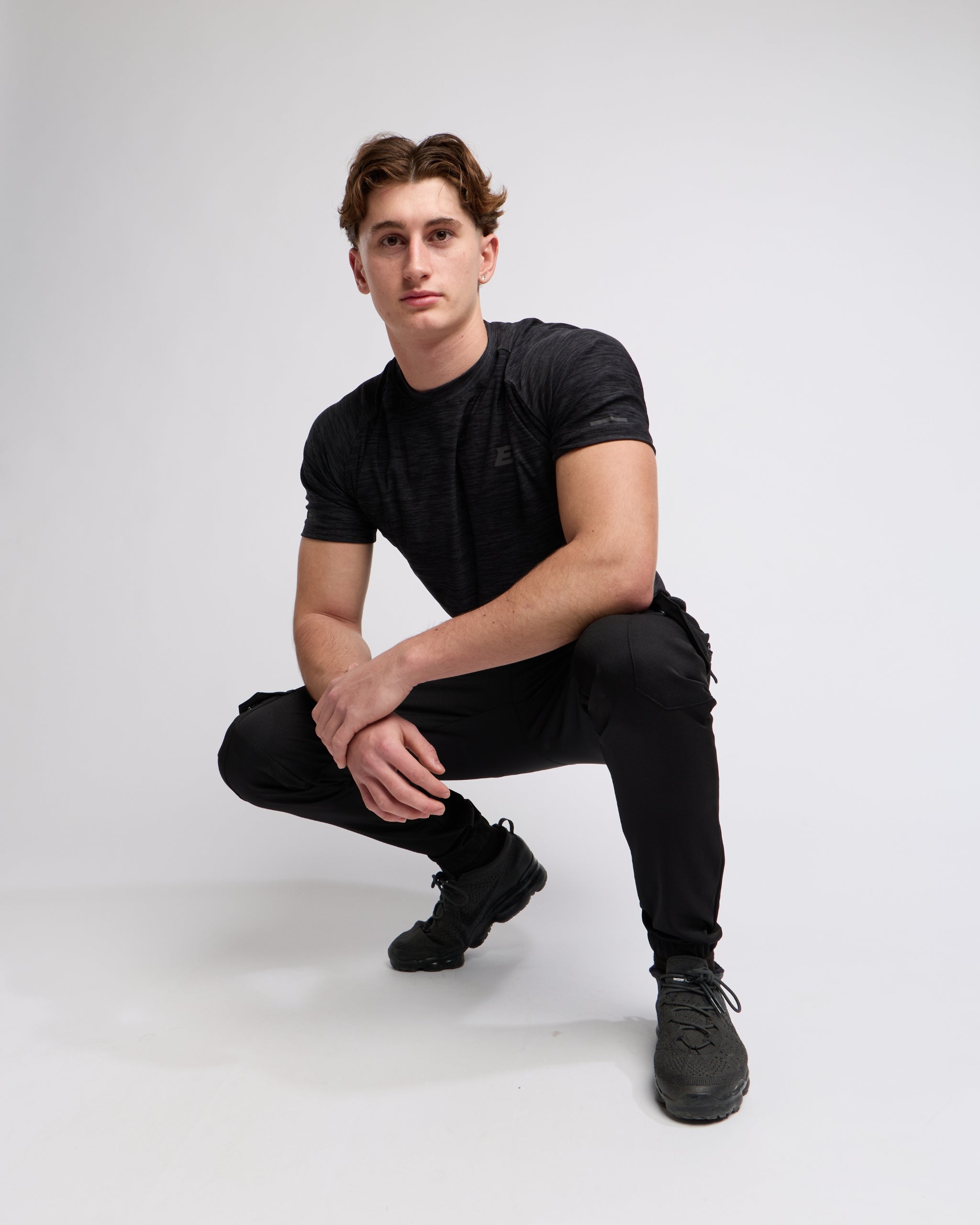 Man wearing a black athletic t-shirt and joggers with a elegante london logo on a light gray background