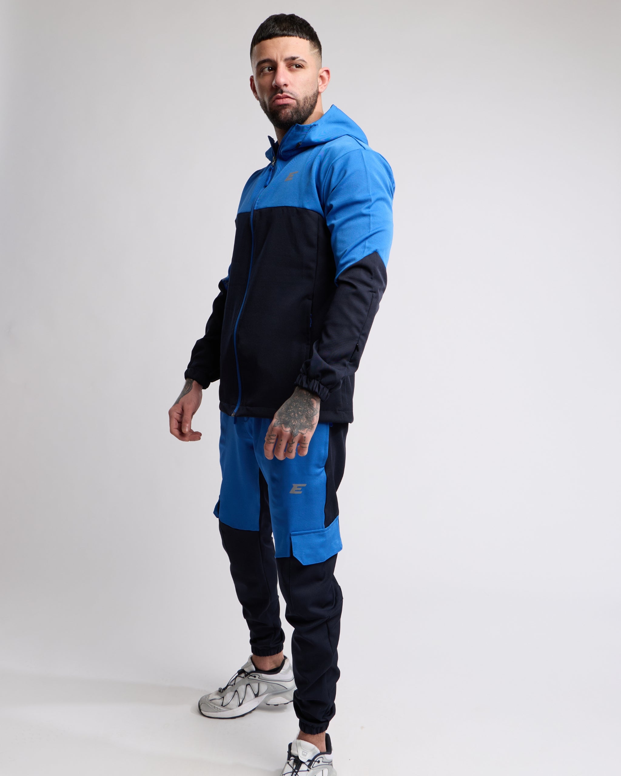 Man wearing a Blue and Navy sports tracksuit jacket with matching tracksuit pants on a white background