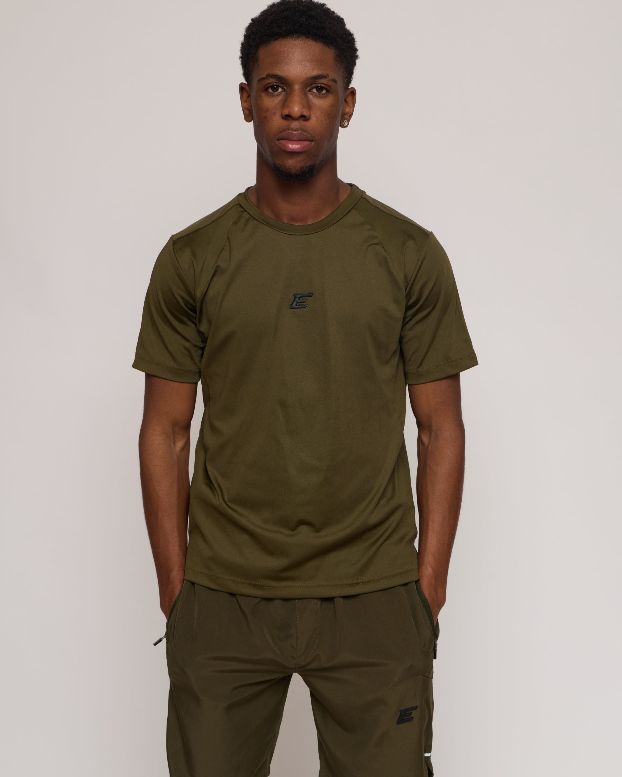 Man wearing a green khaki athletic shorts and t-shirt outfit on white background