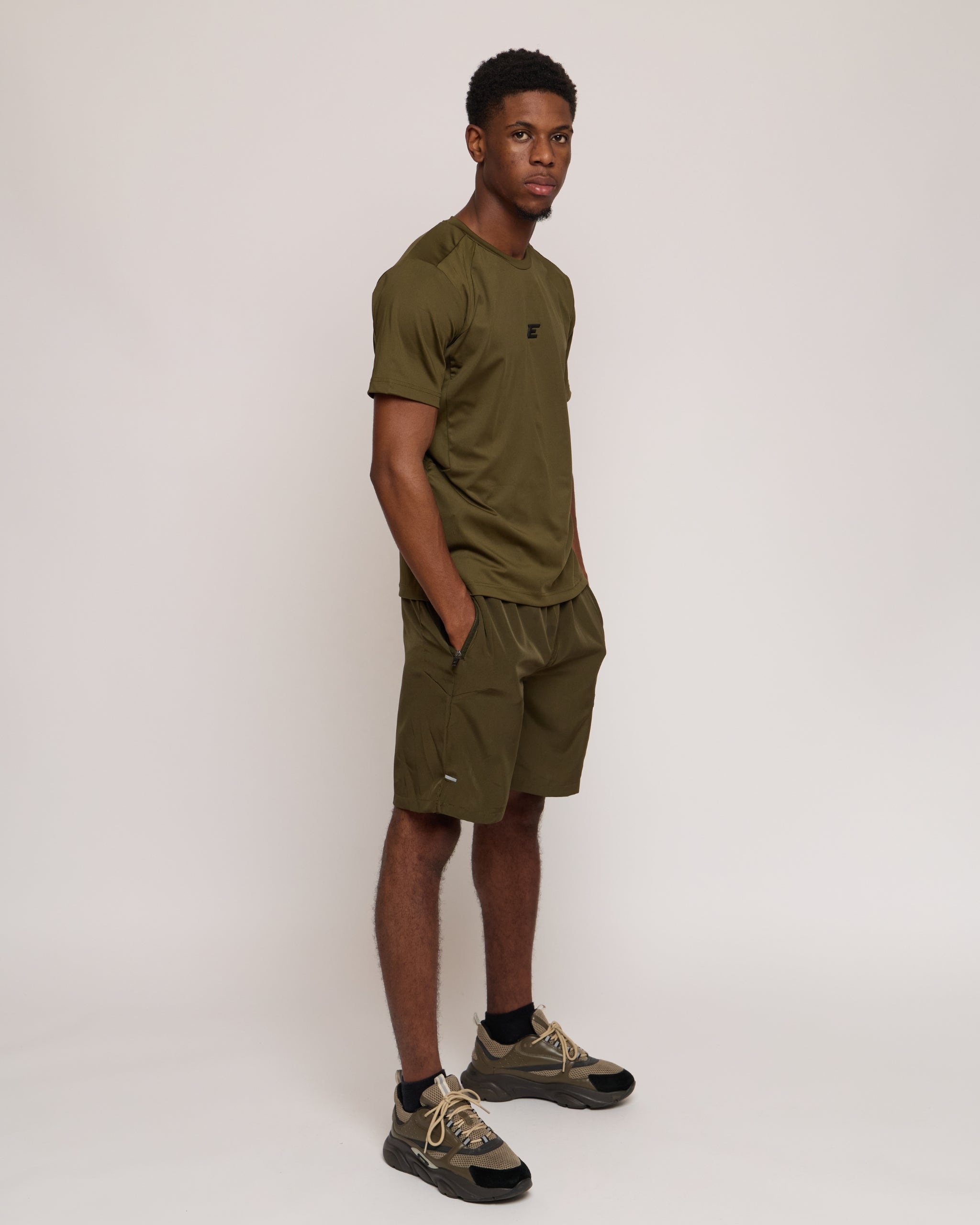 Man wearing a green khaki athletic shorts and t-shirt outfit on white background