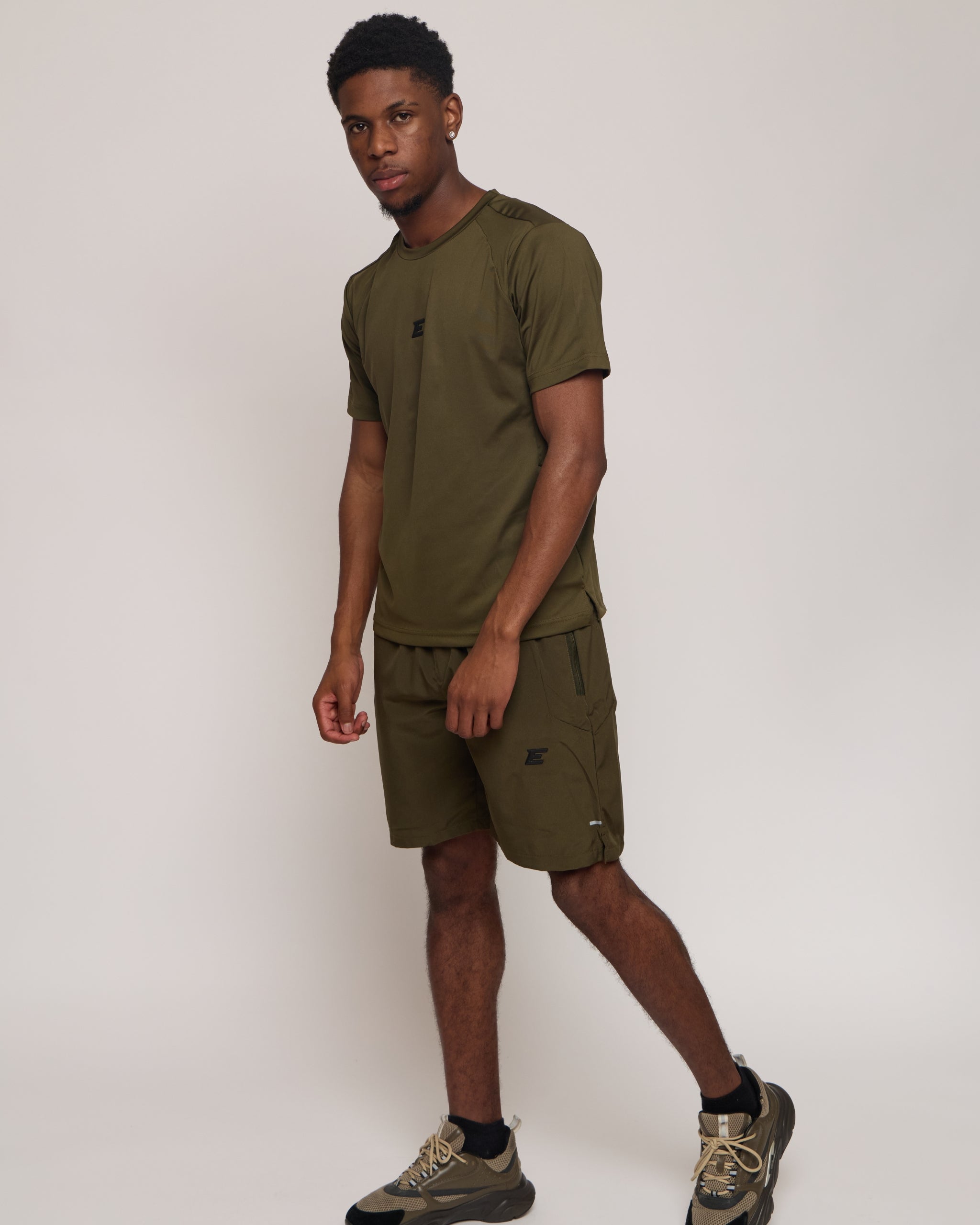 Man wearing a green khaki athletic shorts and t-shirt outfit on white background