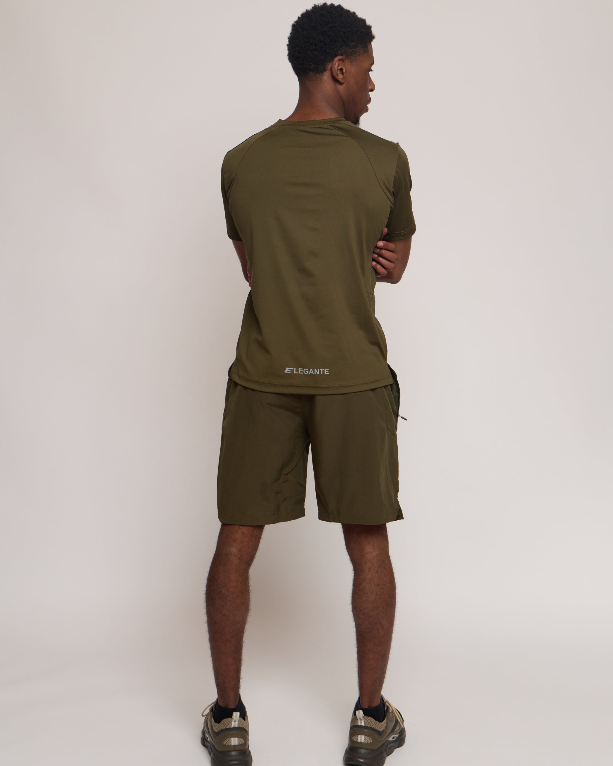 Man wearing a green khaki athletic shorts and t-shirt outfit on white background