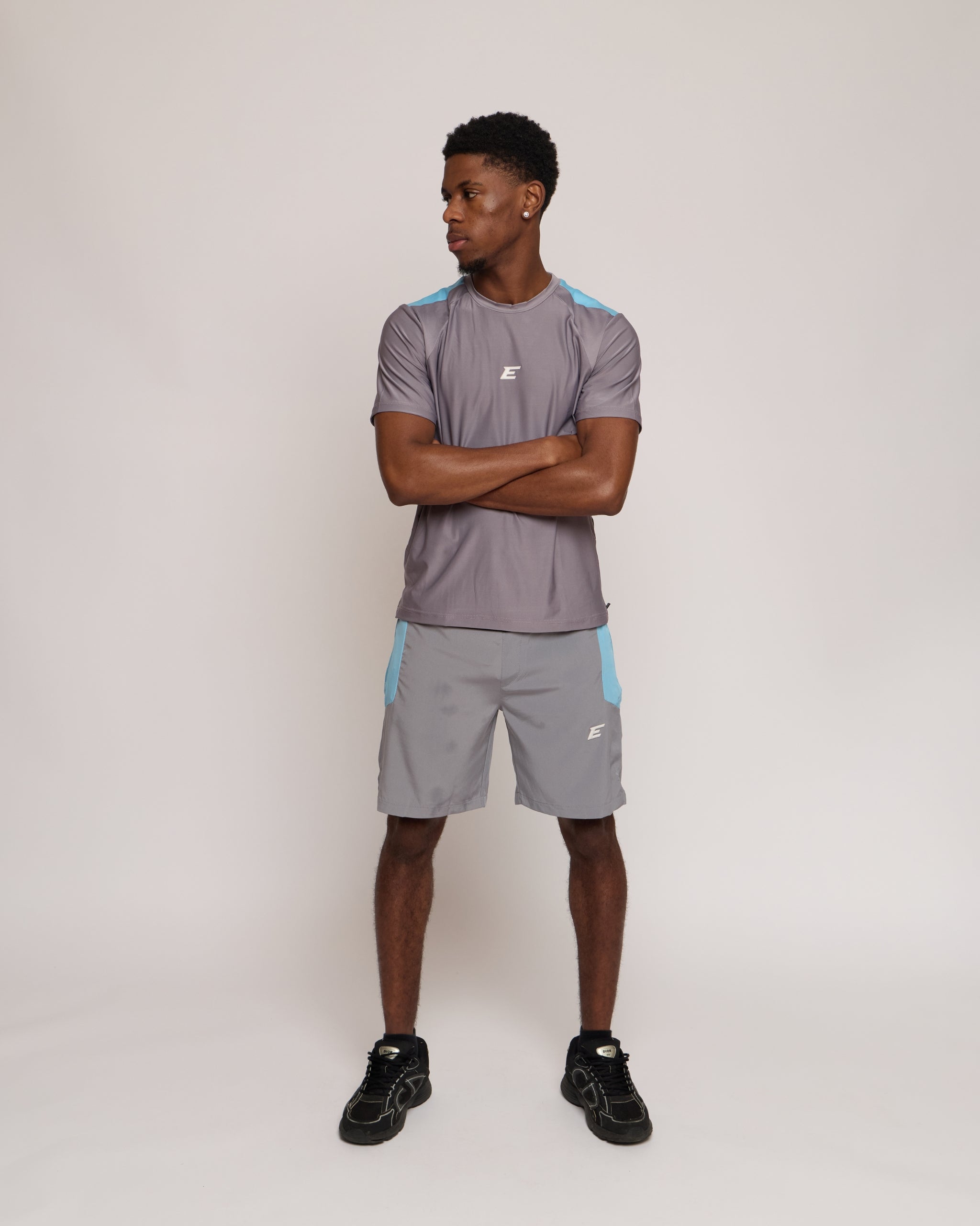 Man wearing a gray athletic shorts and t-shirt outfit with blue accents on a white background