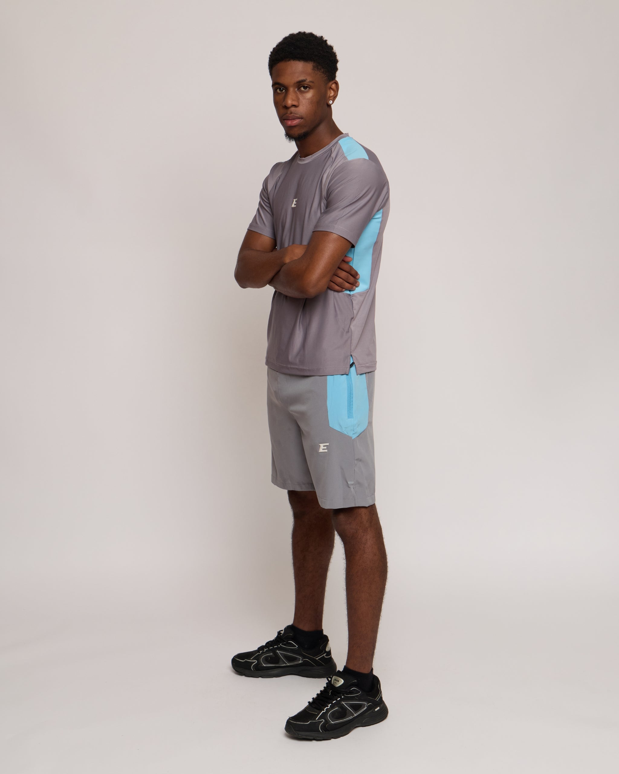Man wearing a gray athletic shorts and t-shirt outfit with blue accents on a white background
